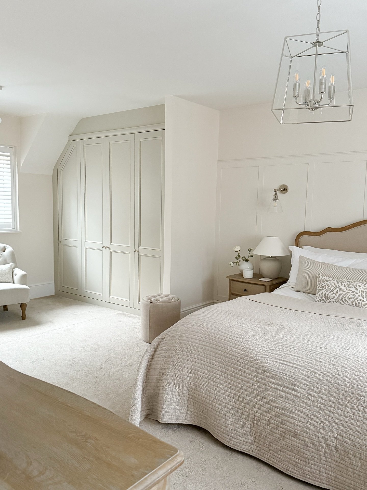 Bespoke pale sage green panel wardrobe custom-fitted into a bedroom corner with a sloped ceiling, featuring silver knobs in a bright, neutral room.
