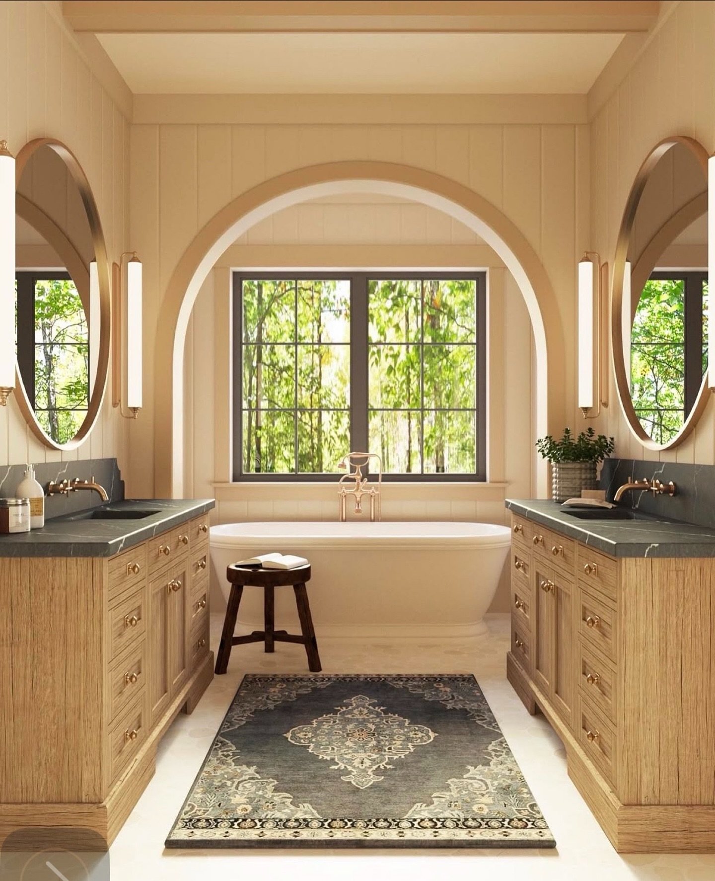 A symmetrical bathroom with light wood dual vanities, dark stone countertops, two oval mirrors, and a rectangular gray and cream medallion-patterned rug placed between the vanities.