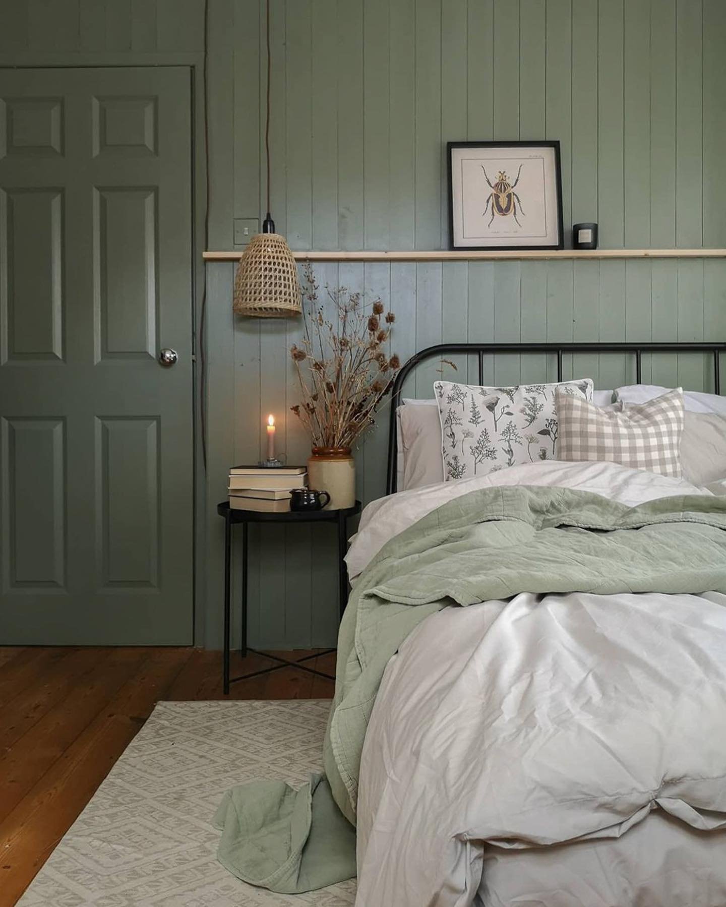 Bedroom featuring a rustic vertical paneled sage green wall, dark wood floors, and soft grey bedding.