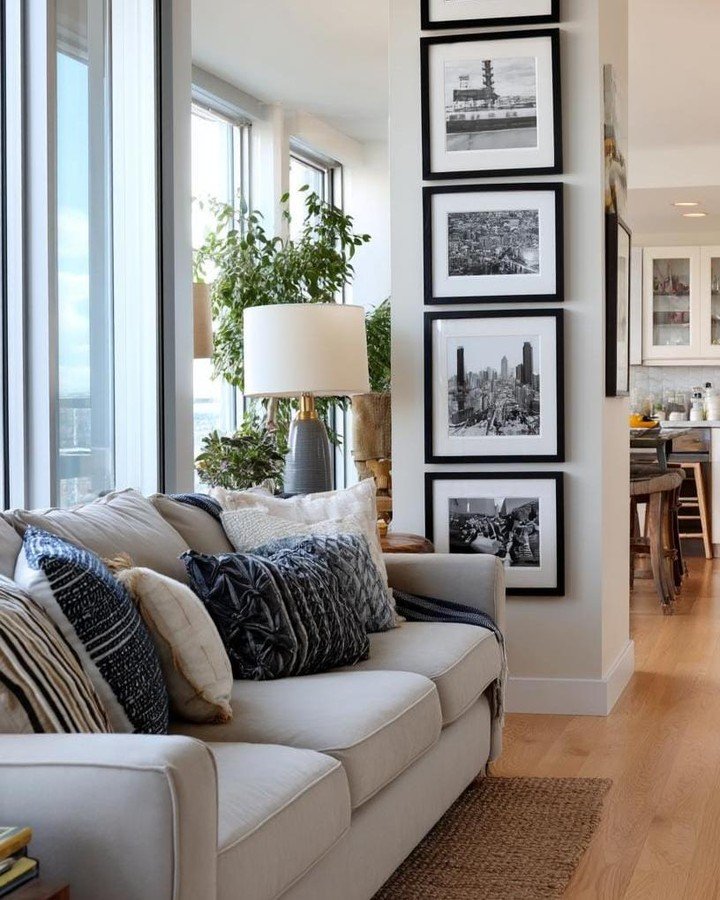 Vertical stack of four black-framed black and white cityscape photographs hung on a narrow wall next to a beige sofa in a high-rise apartment.
