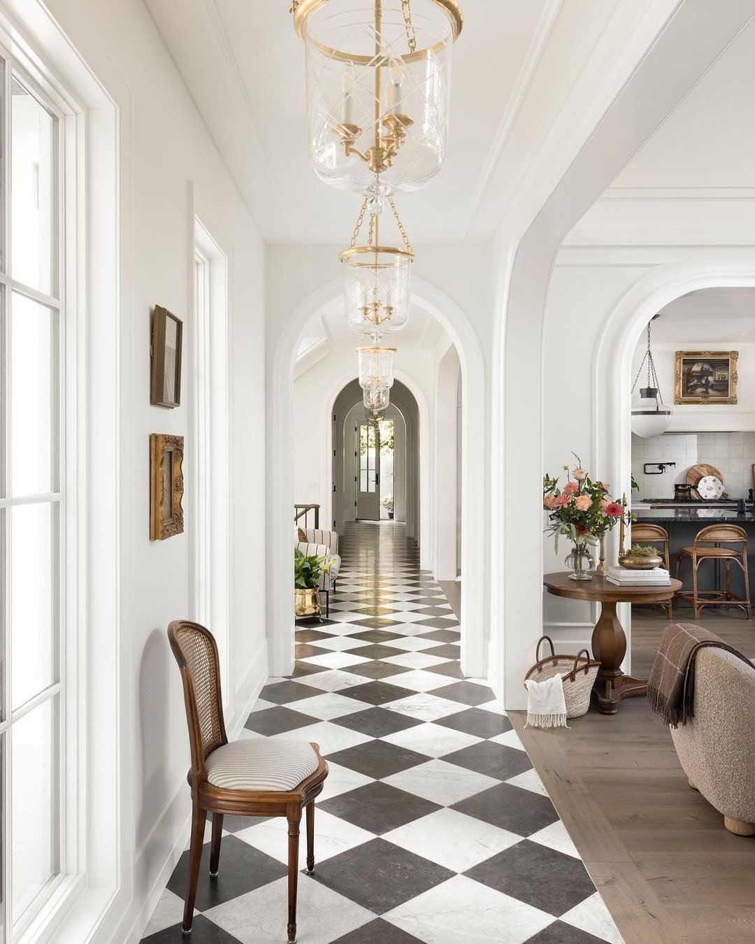 Bright hallway with white walls and trim, black and white diamond marble flooring, and three tiered, clear glass and gold metal lantern pendants.