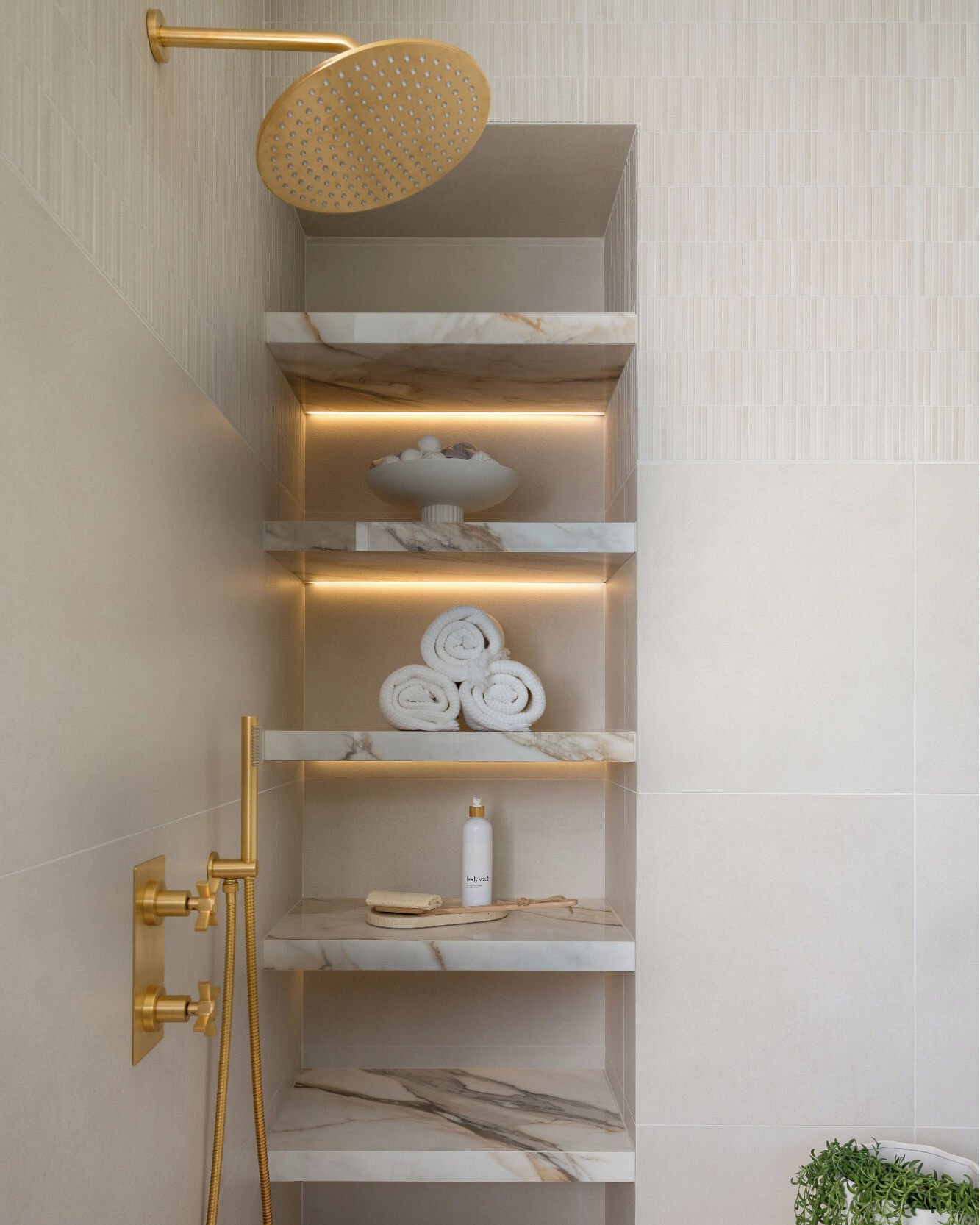 Four built-in shelves made of white and gold-veined marble with hidden LED strip lighting installed beneath the top two shelves.