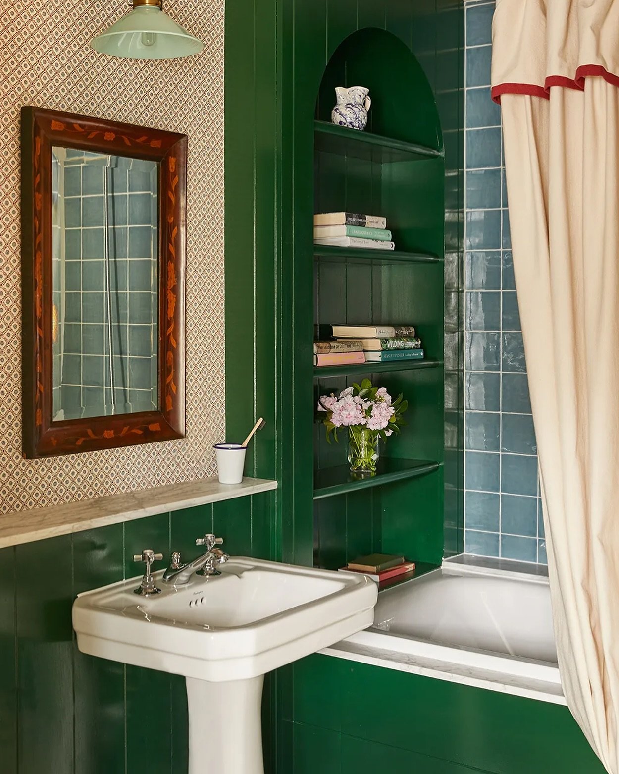 A tall, slender built-in shelving unit painted bright emerald green, featuring four shelves holding books and a small floral arrangement.