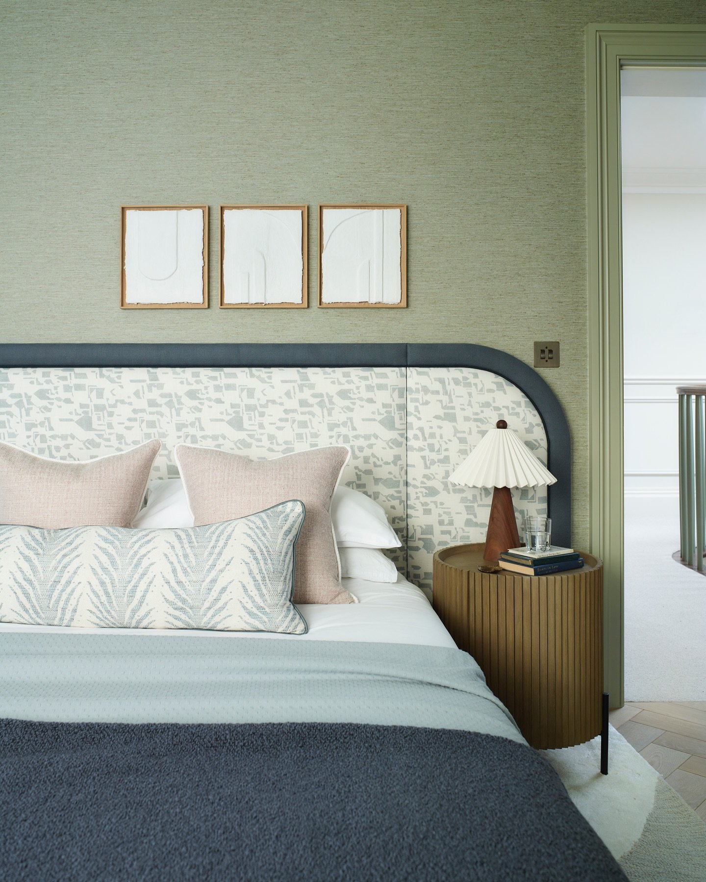 Wide, custom-fit headboard upholstered in a pale grey abstract patterned fabric, with a dark blue border that curves gracefully at the top corners against a textured green wall.