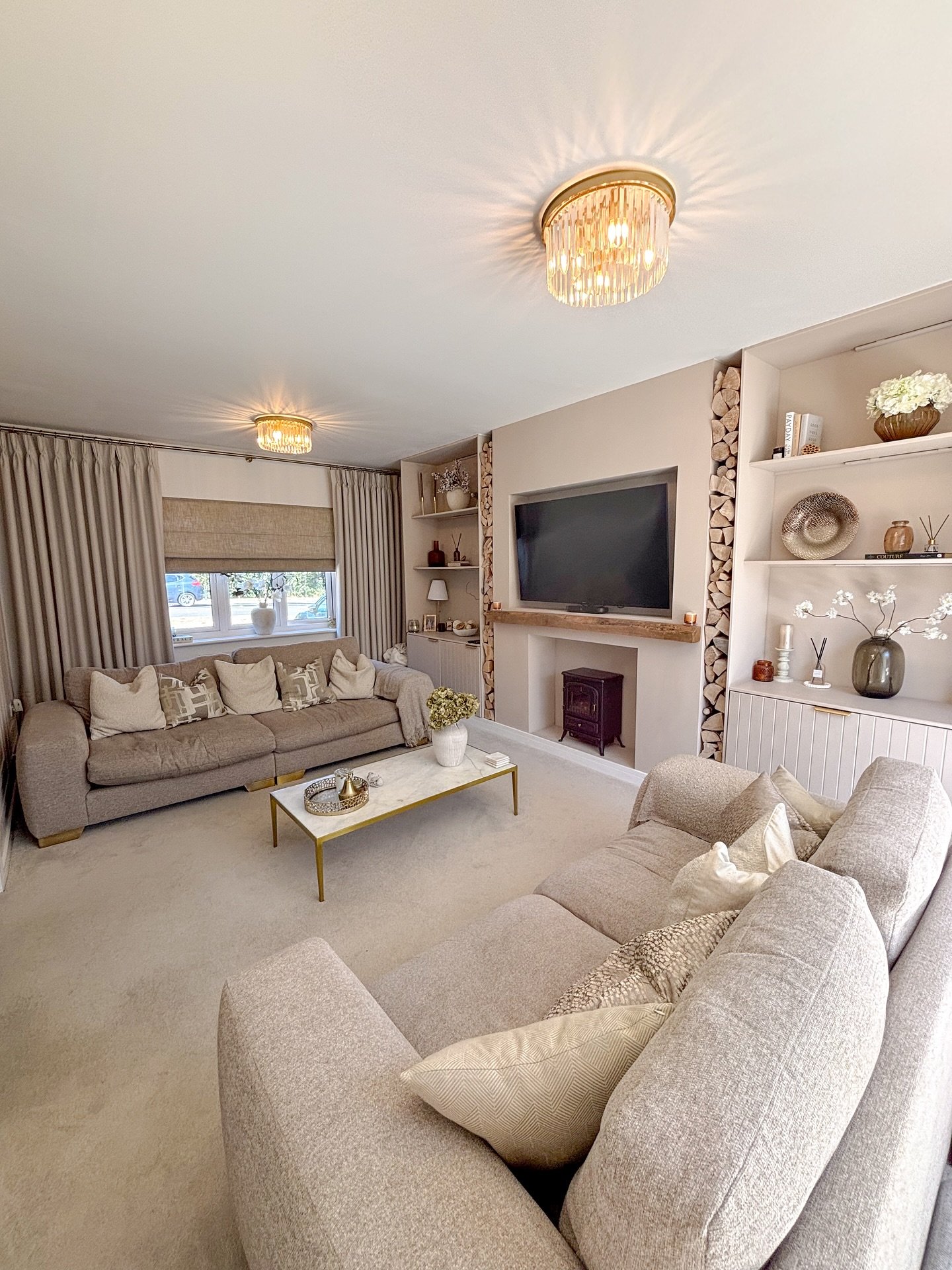 Living room with two neutral fabric sofas, built-in shelving, a small wood burner, and crystal flush-mount lighting.