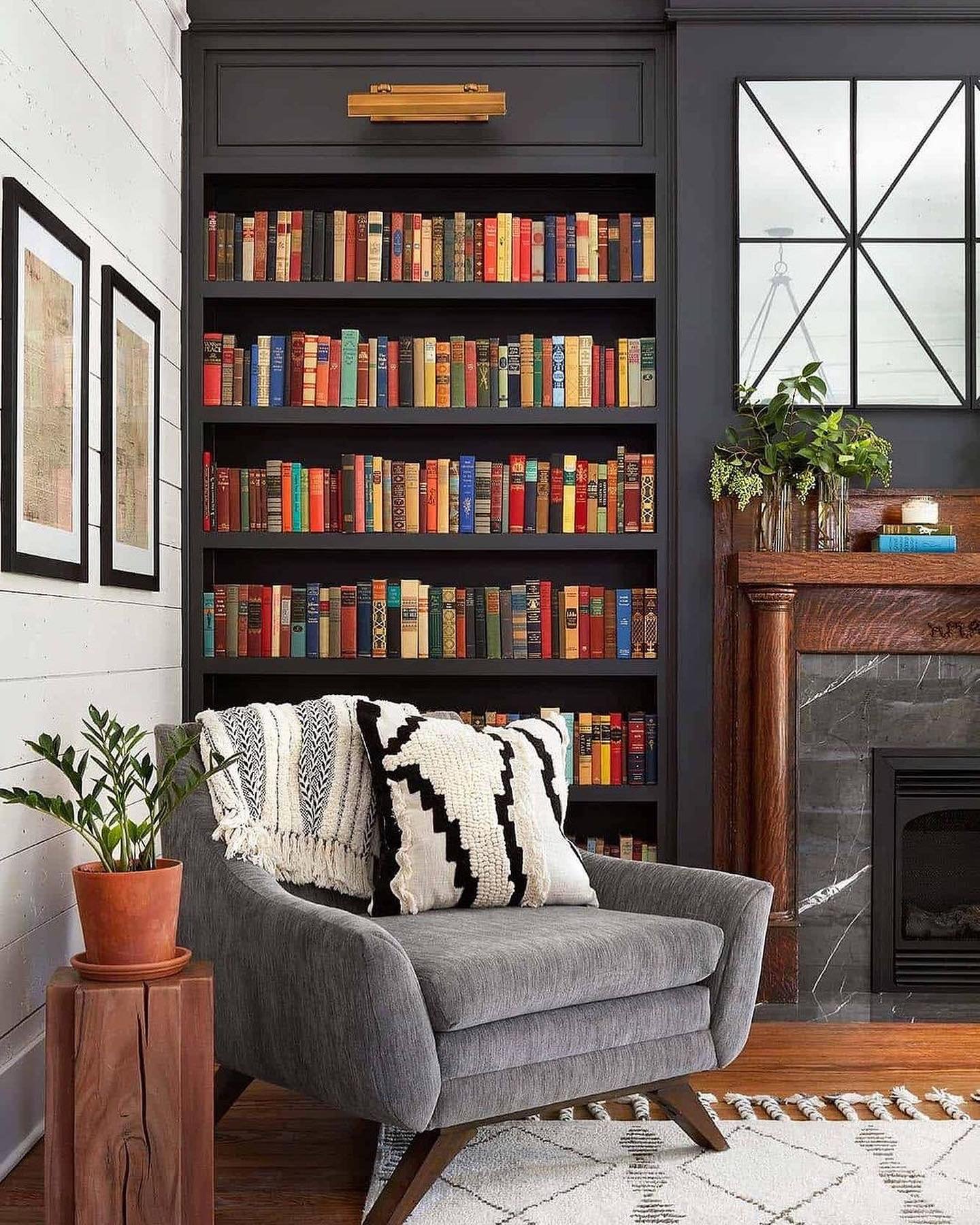 Reading corner with a dark gray velvet armchair, a black built-in bookcase filled with colorful books, and a rustic wood side table.