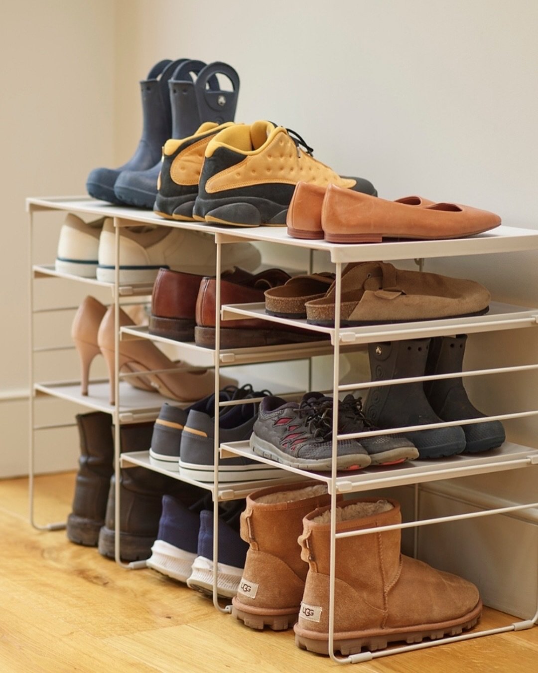 Several white wire-frame racks stacked vertically, holding various types of shoes including boots and flats.