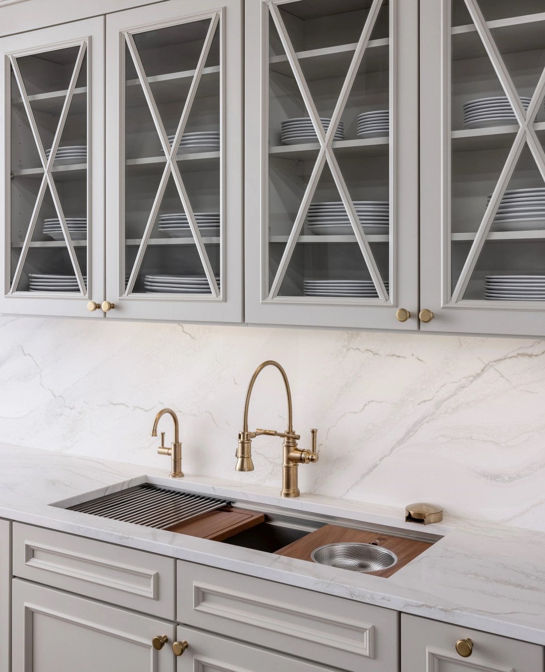 A contemporary dark gray undermount kitchen sink featuring integrated accessories like a wooden cutting board and metal grid, paired with antique brass faucets.