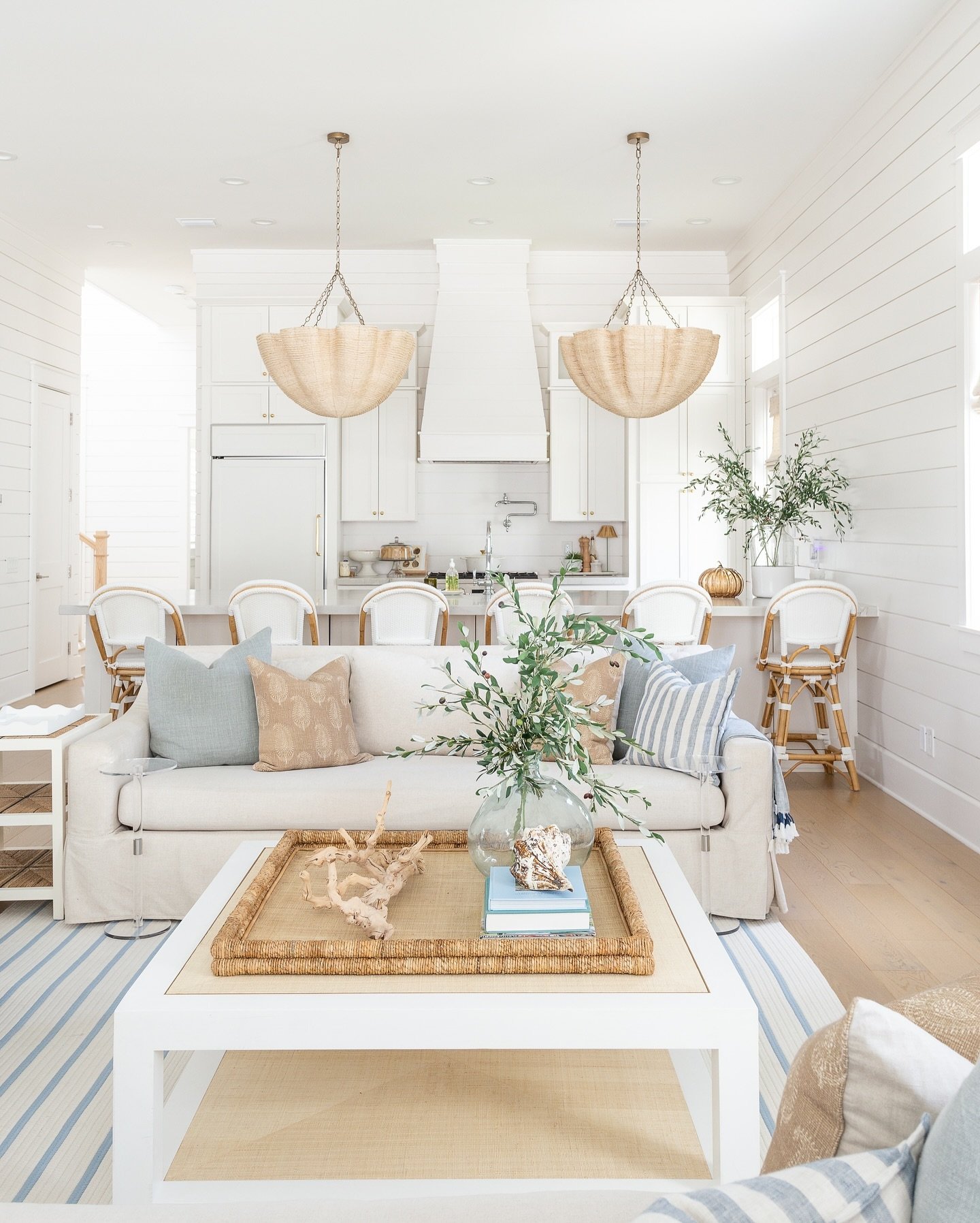A bright, open-concept living space with shiplap walls, a slipcovered white sofa, blue and beige throw pillows, and light blue striped area rug.
