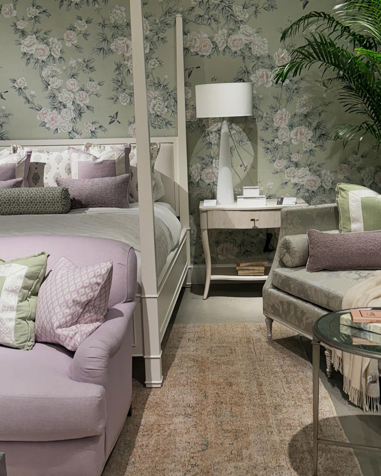 Luxurious bedroom featuring a sage green and pink floral wallpaper, a white four-poster bed, and lavender seating.