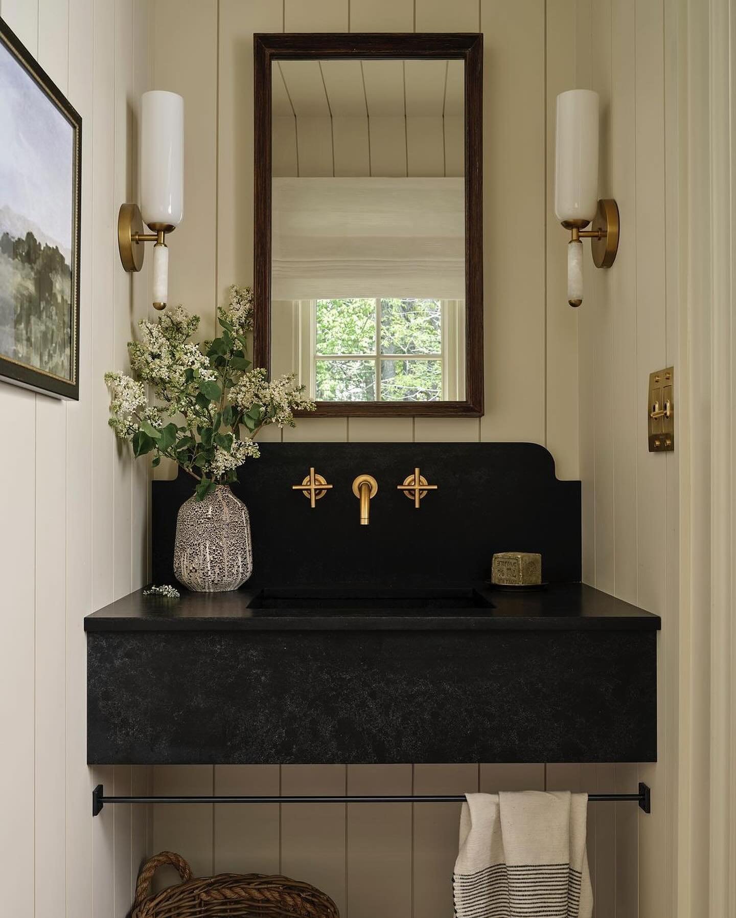 Black stone console sink with black basin and a bronze towel bar, set against light beige vertical shiplap paneling.