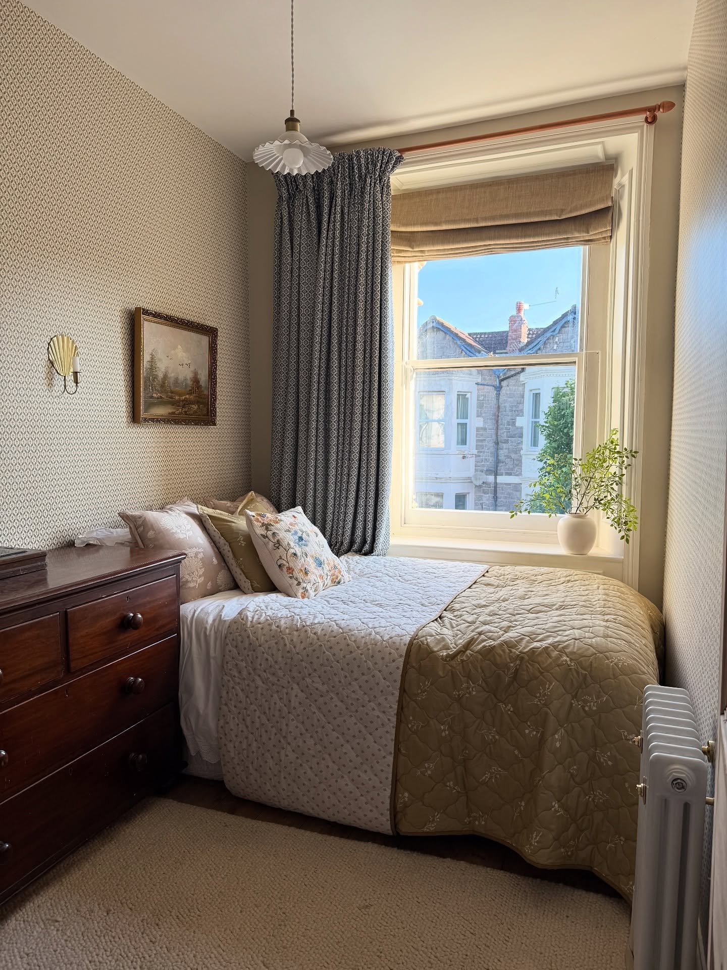 Dark patterned curtain paired with a natural tan Roman shade in a small bedroom.
