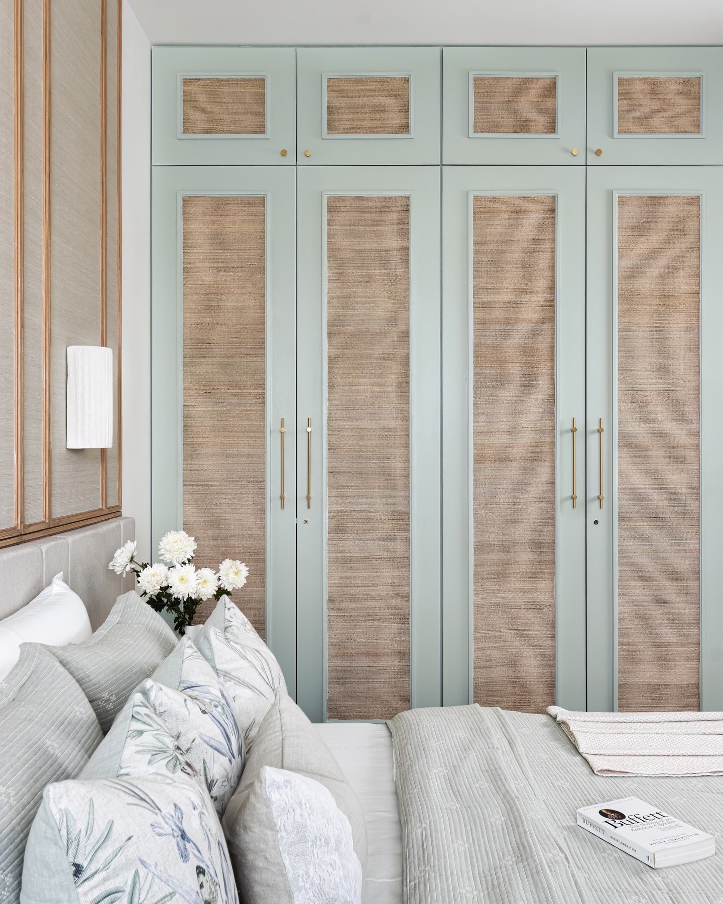 Custom-built wardrobe in a calming mint green color with rectangular panels of woven rattan or cane webbing, finished with brass hardware.