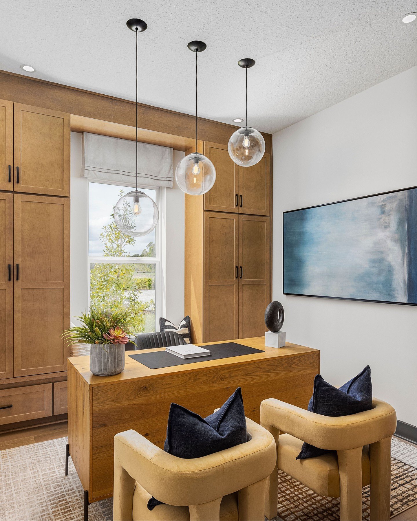 Executive home office with warm, honey-toned wood built-in cabinets, a matching wooden desk, and two mustard-yellow chairs with navy pillows.
