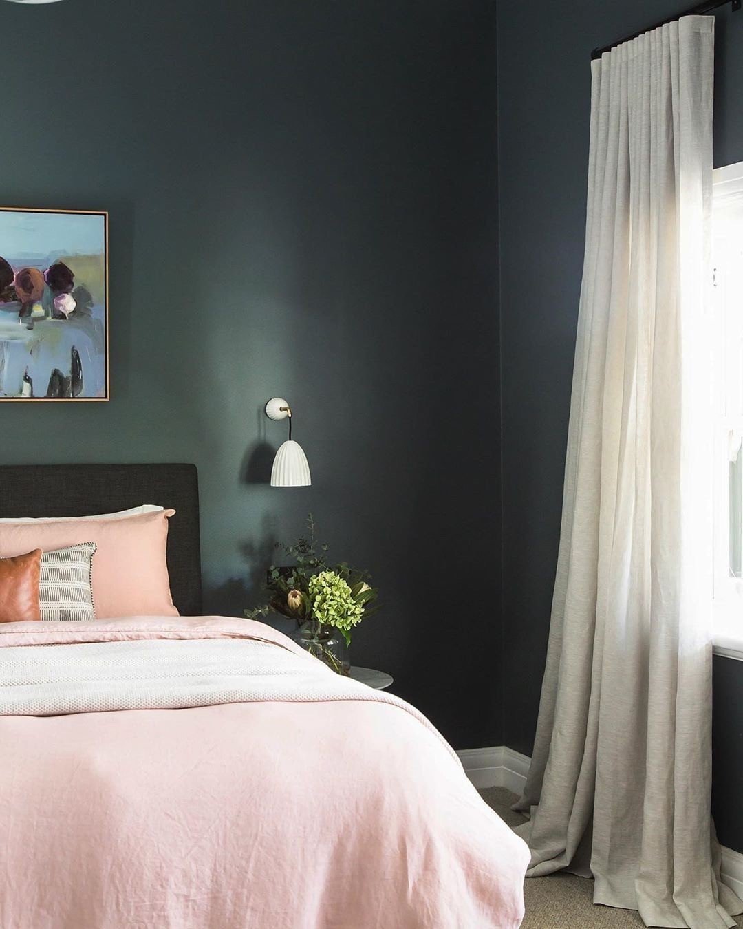 A bedroom featuring a dark emerald green accent wall with decorative molding, a bed with light bedding, and pampas grass decor.