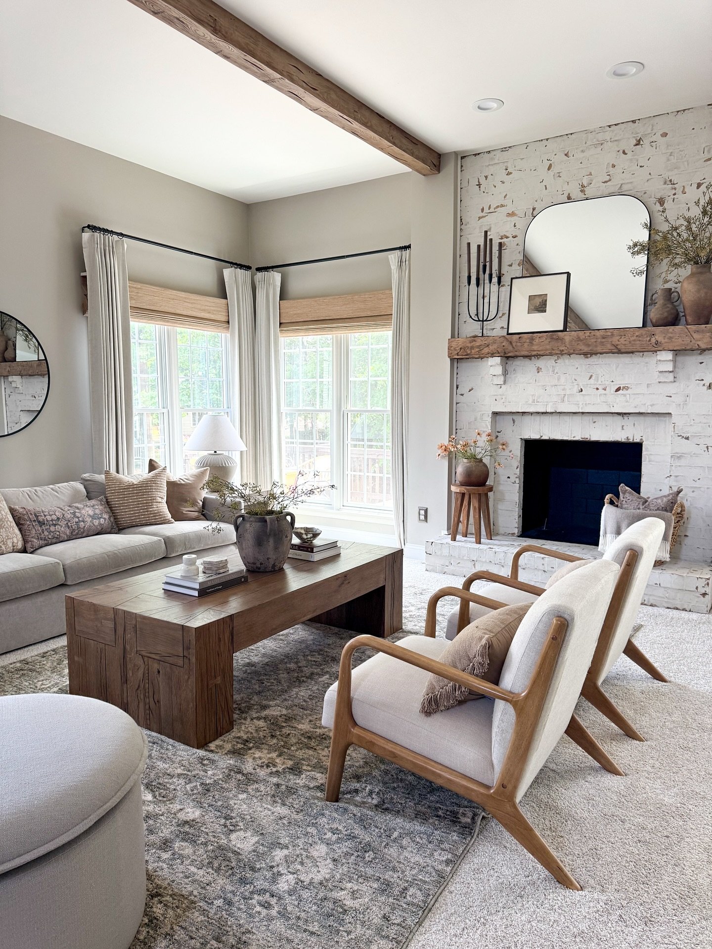 A neutral living room showcasing a white-washed exposed brick fireplace, rustic wood beams, and a chunky wood coffee table.