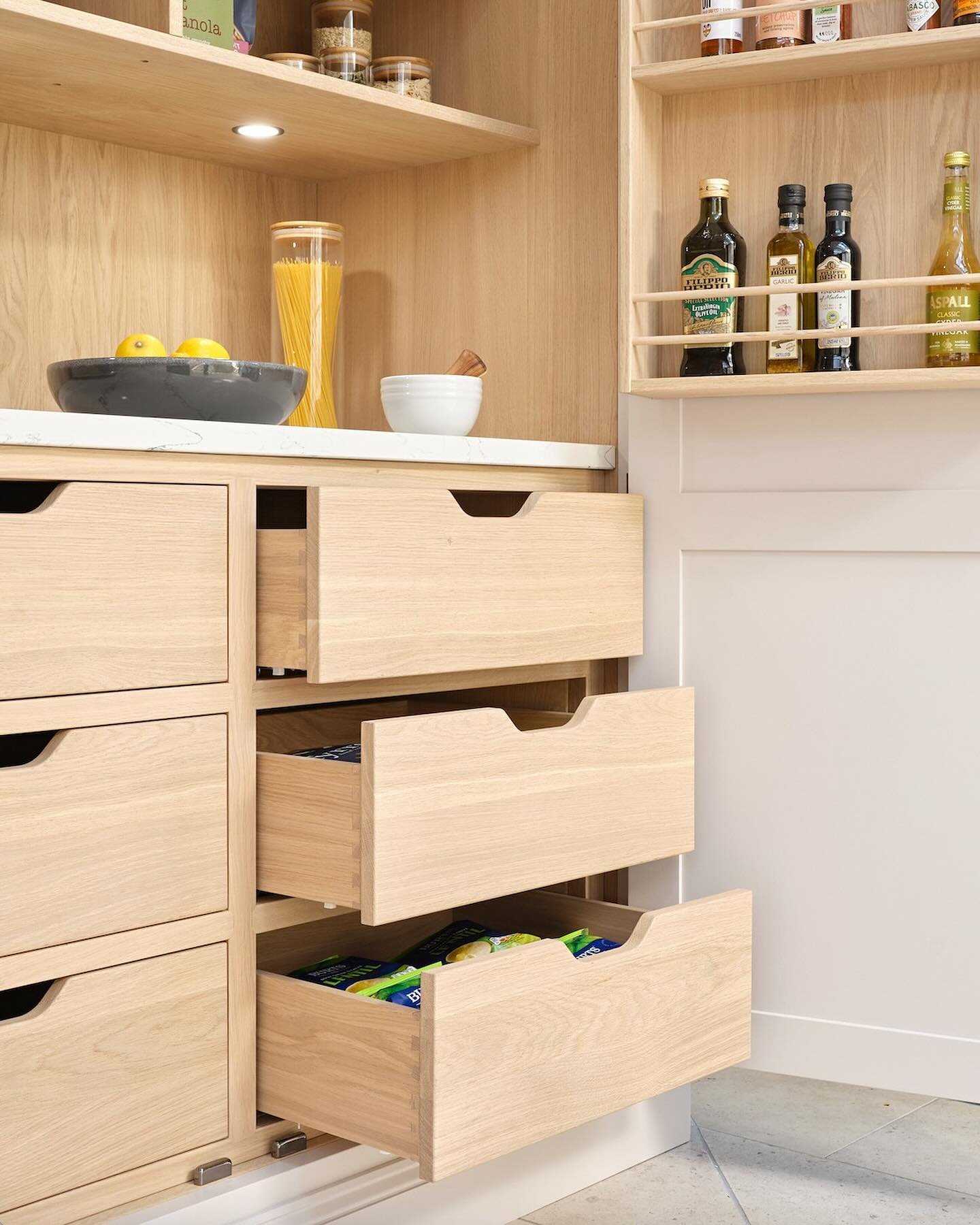Custom pantry cabinet with multiple pull-out drawers made of light natural oak wood and finger pulls.