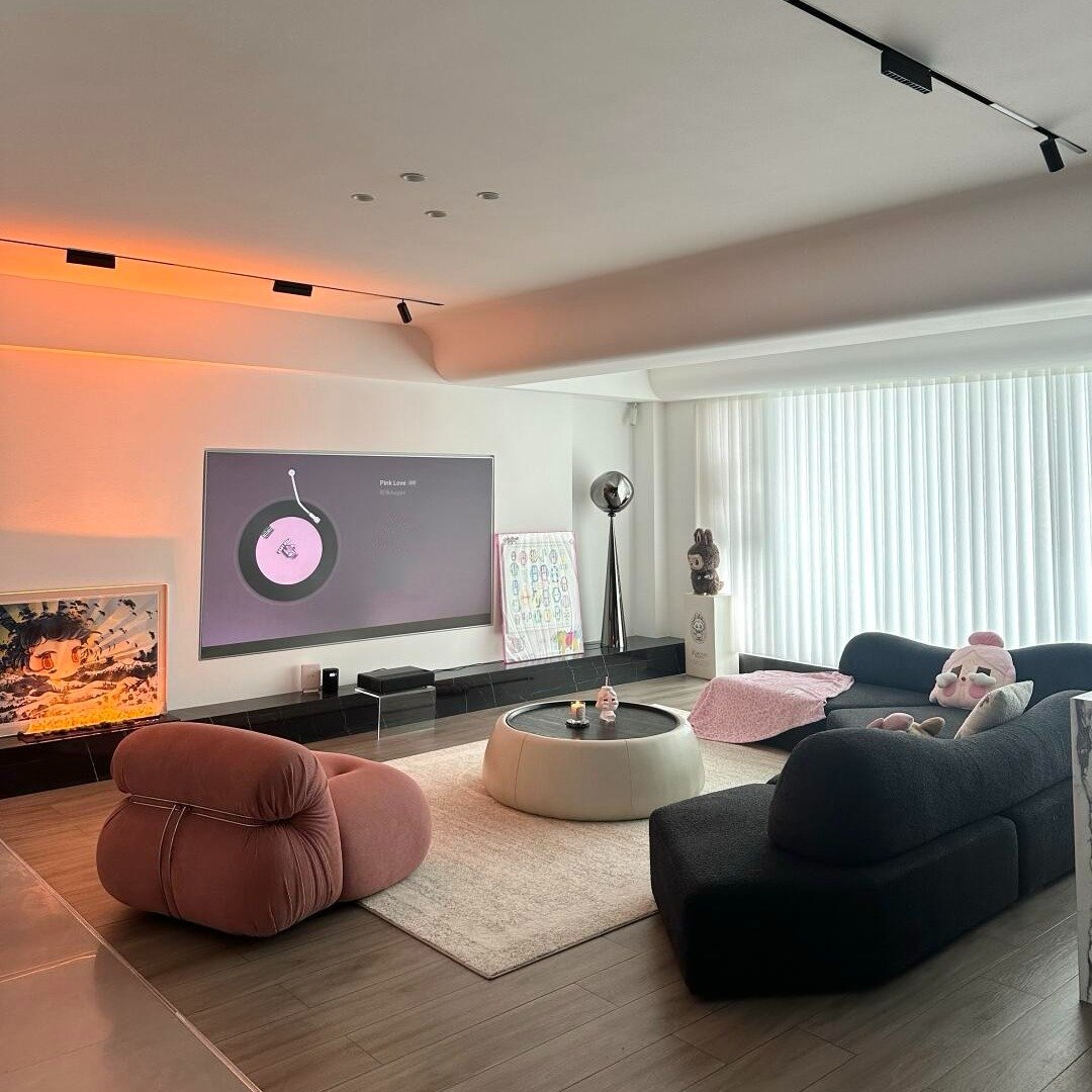 Modern lounge with dark curved sofas, a pink velvet chair, a projection screen, and bright orange accent lighting.