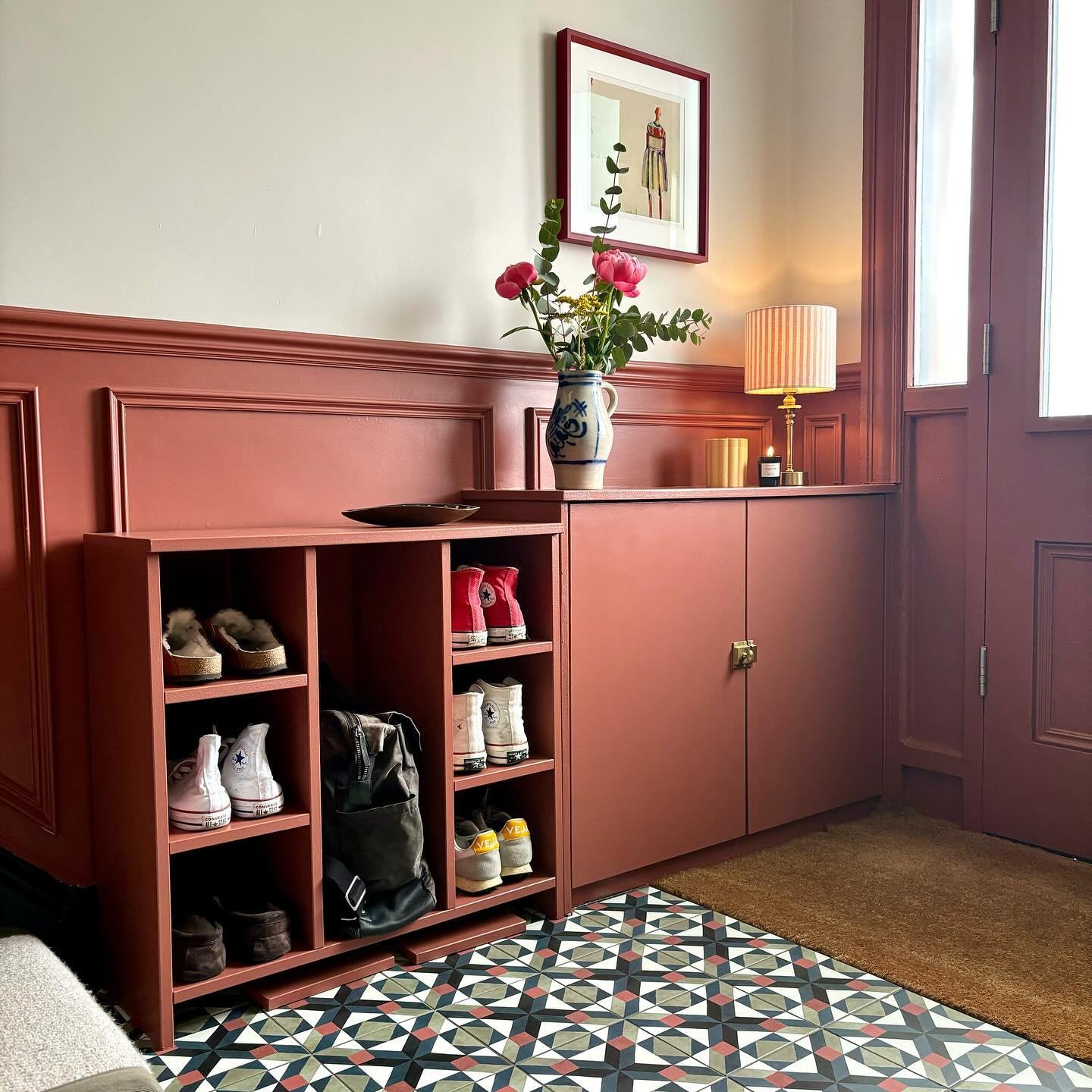 Custom painted terracotta entryway unit with open cubbies for shoes and a closed cabinet next to it.