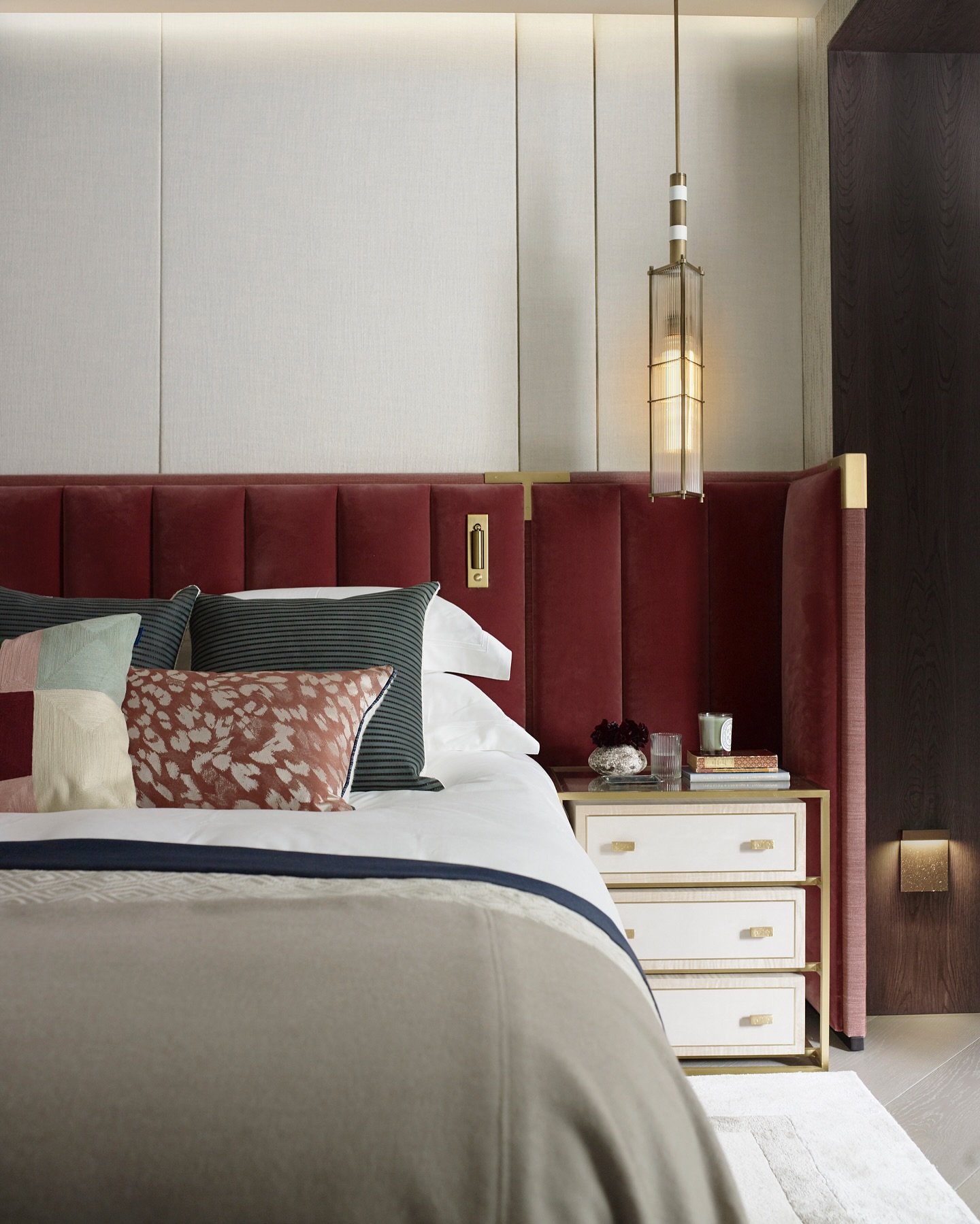 Tall, deep red velvet headboard with vertical channel tufting and high, winged sides, accented with brass detailing and set against a light-colored wall paneling.