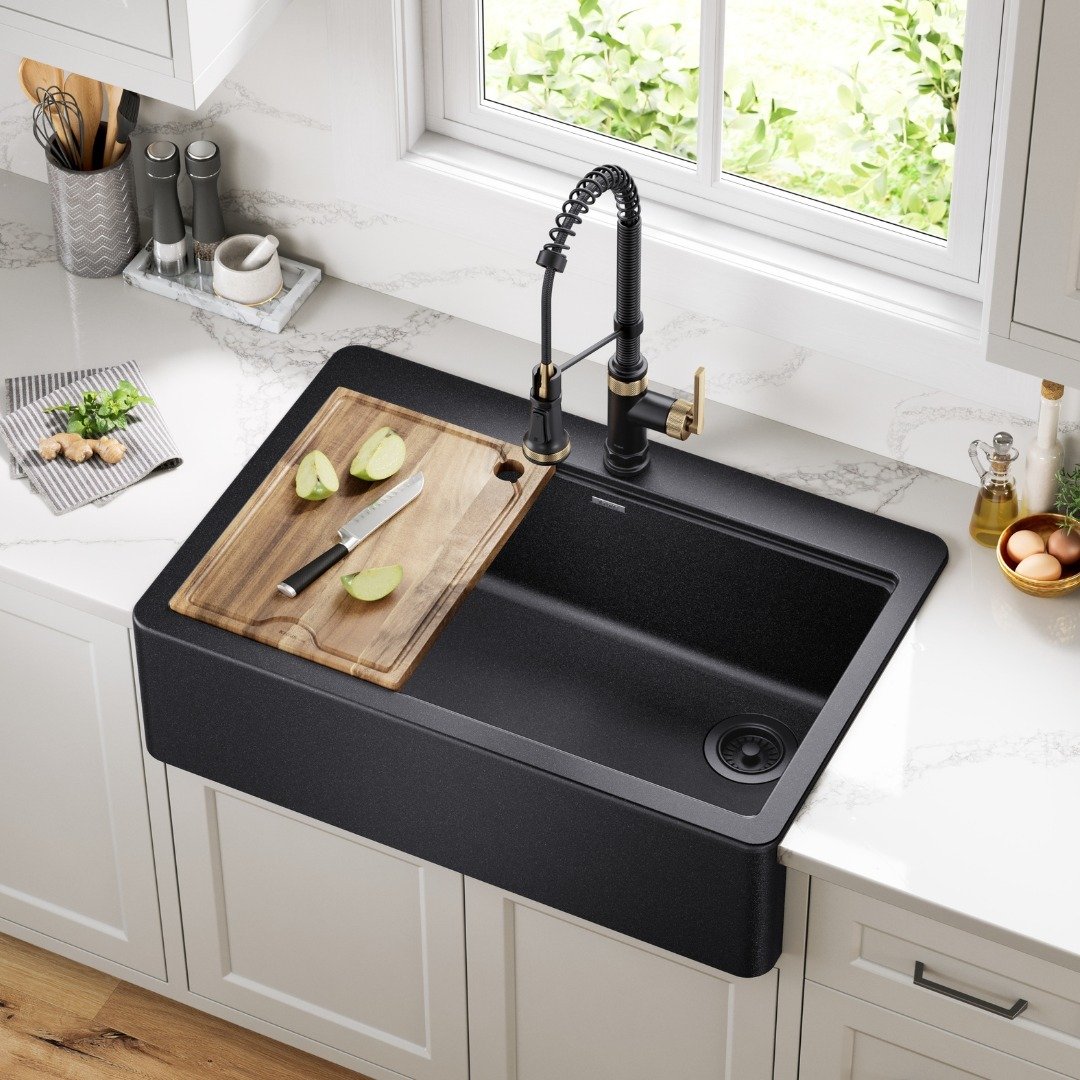 A contemporary matte black single-bowl apron-front (farmhouse) kitchen sink with a wooden cutting board accessory, paired with a black and brass pull-down faucet.