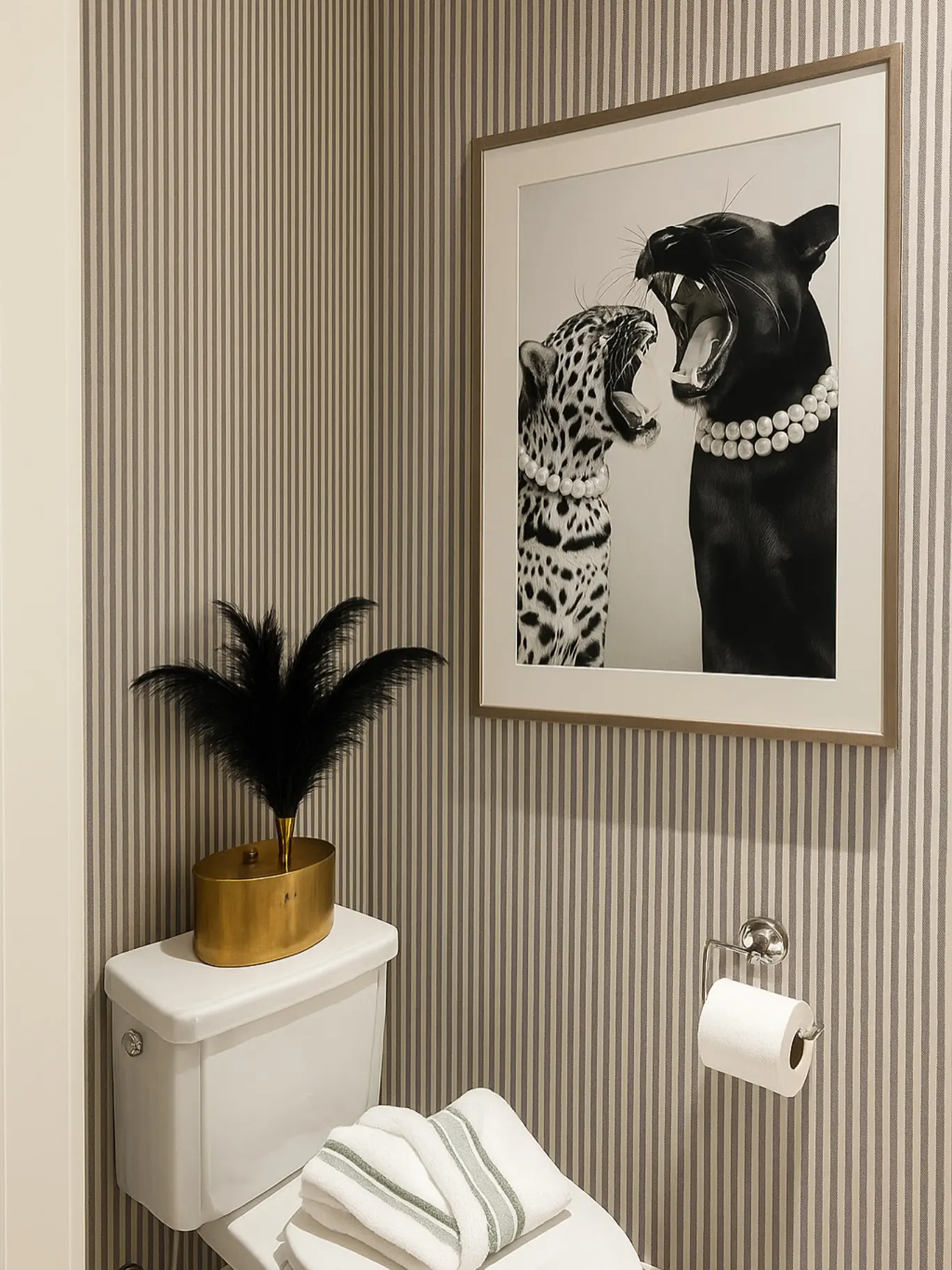 A framed black and white photograph of two big cats wearing pearl necklaces and roaring, hanging over a toilet in a striped wallpapered room.