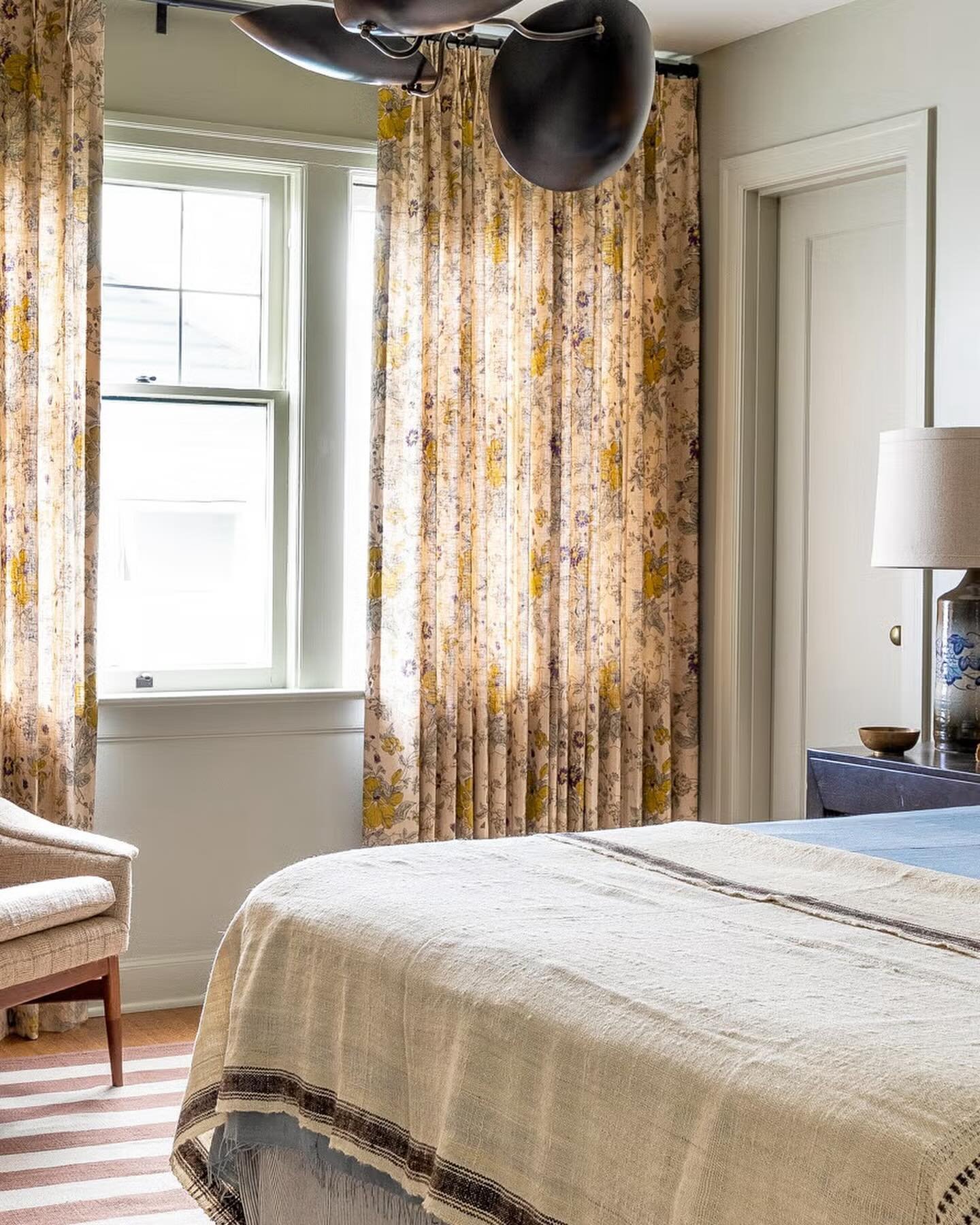 Cream floral print curtains with yellow flowers hang in a sun-drenched bedroom.