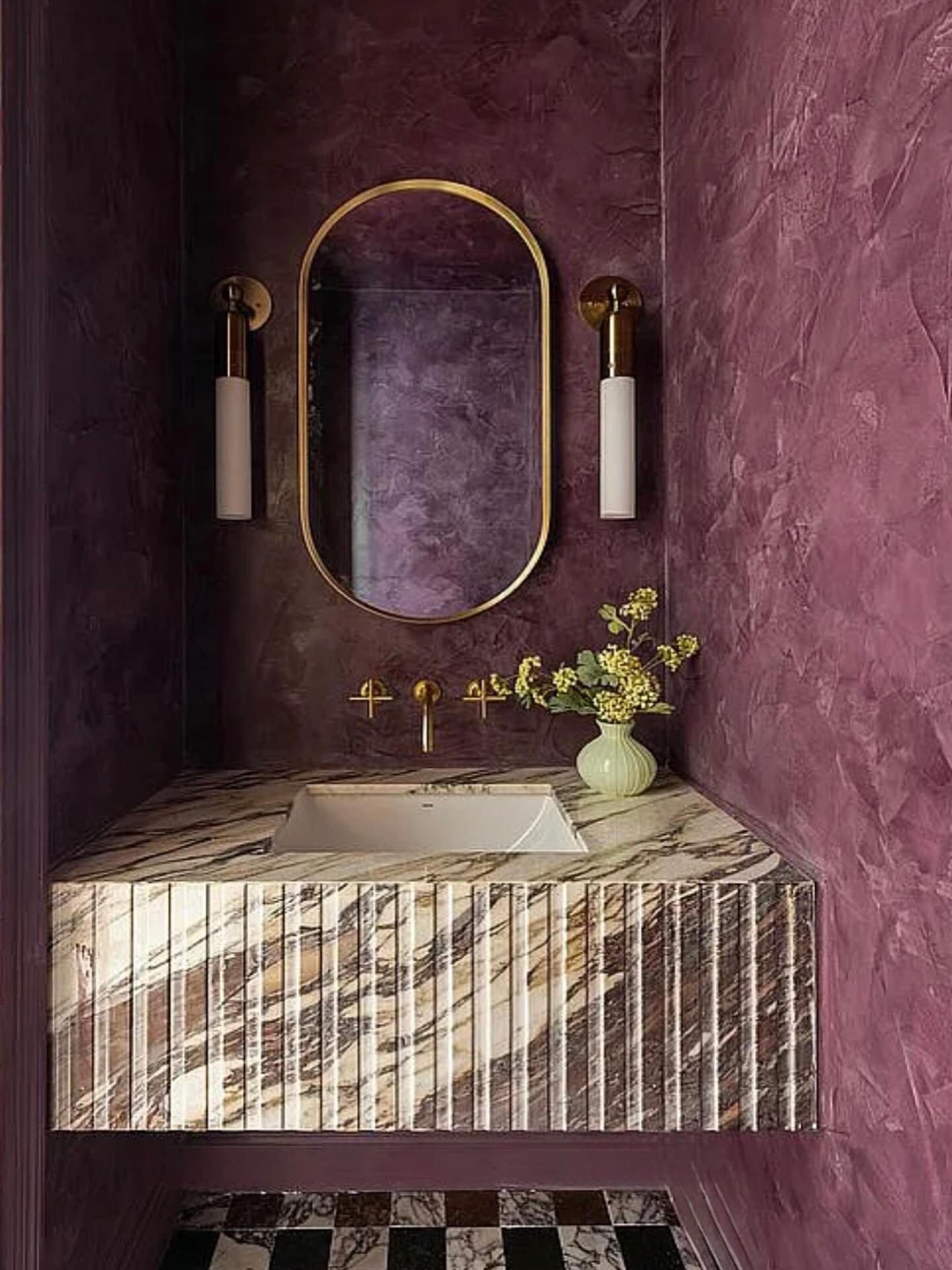 Fluted purple-toned marble vanity in a powder room with deep plum, textured walls and a gold oval mirror.