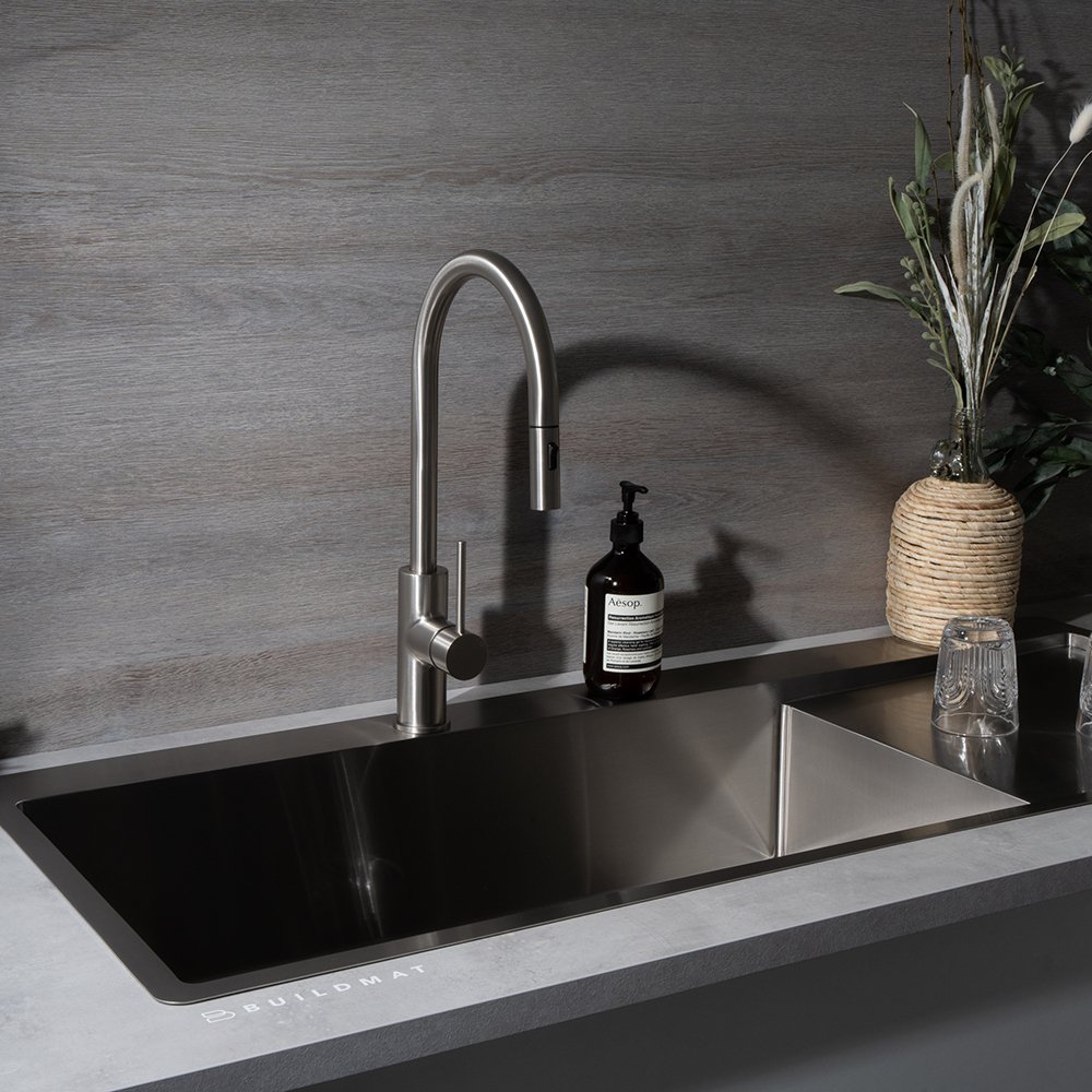 A wide, low-profile stainless steel single-bowl kitchen sink seamlessly integrated into a gray countertop with a brushed nickel high-arc faucet.