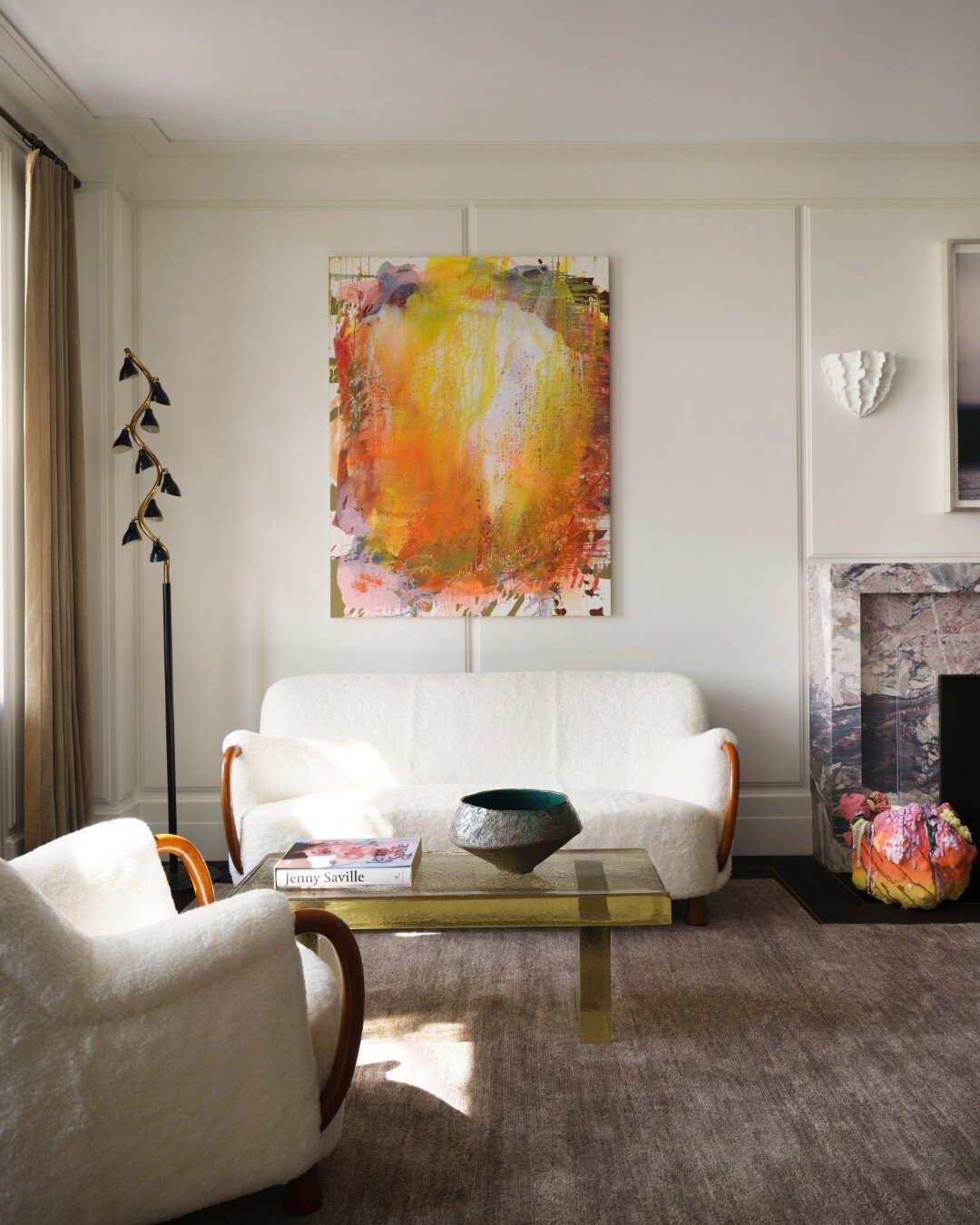 Large vertical abstract painting in bright yellow, orange, and red tones, hung above a white curved settee in a classic white living room.