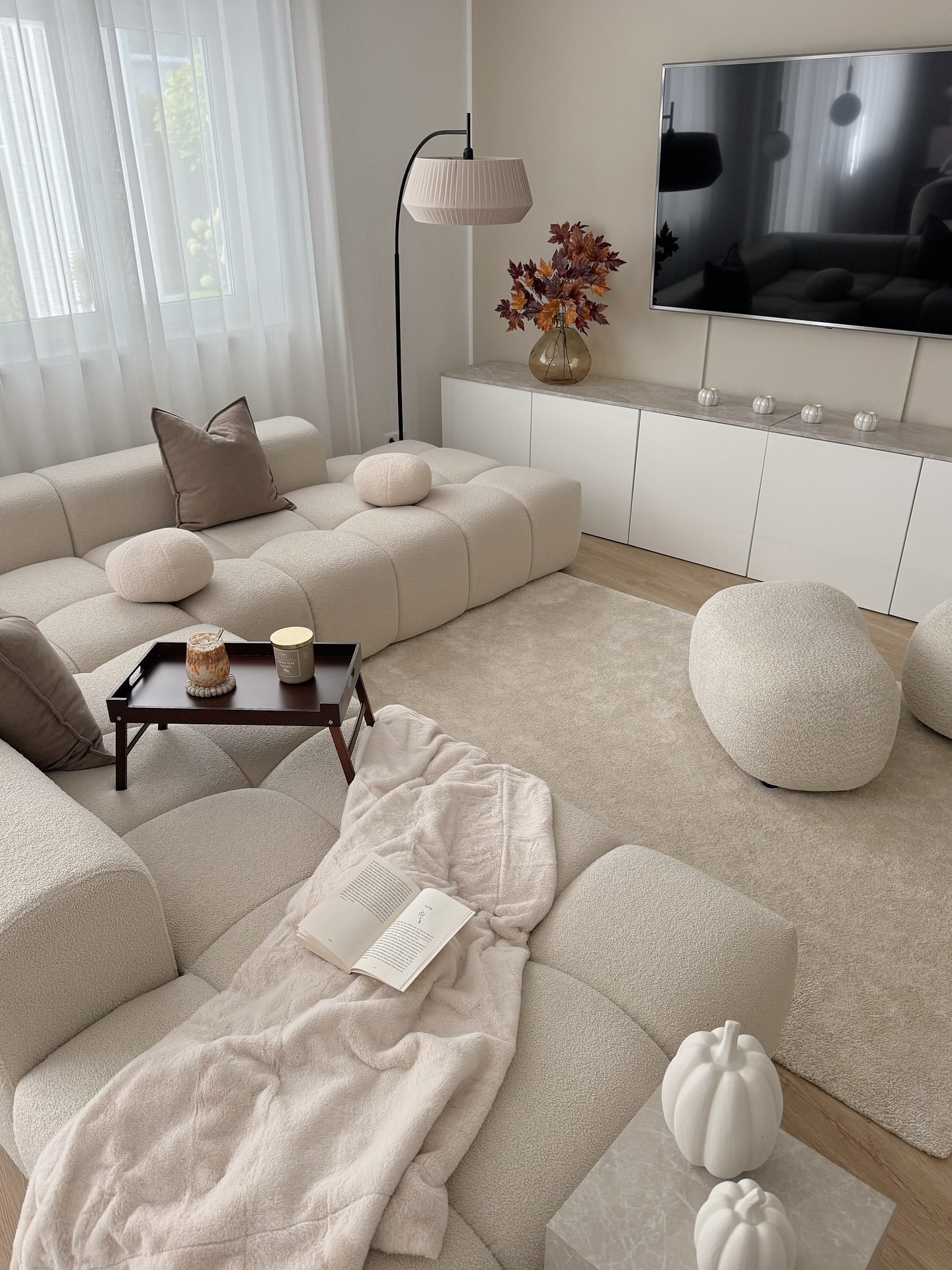 A cozy, neutral living room with a large, tufted modular bouclé sectional, low white storage cabinets, and a matching textured rug and ottoman.
