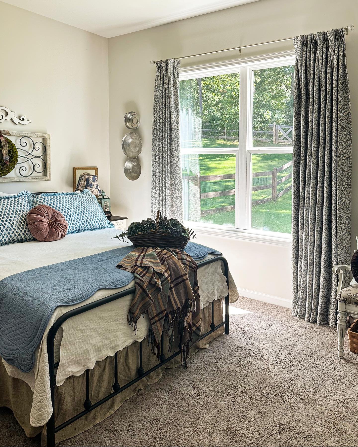 Gray and white patterned curtains framing a window overlooking a green yard in a cozy bedroom.