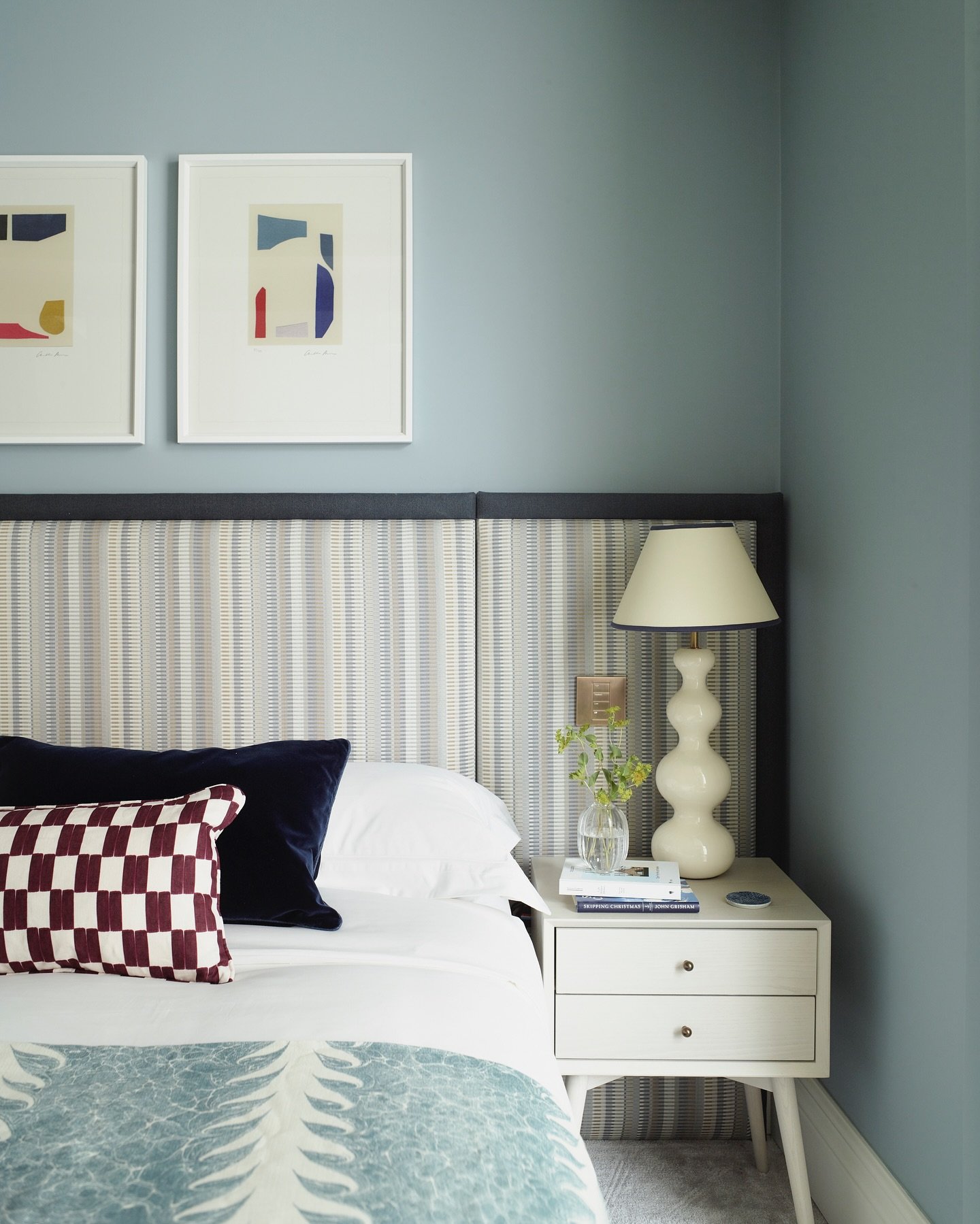 Wide, tall upholstered headboard featuring a subtle vertical stripe pattern in light blue and beige, framed by a solid navy blue border against a matte blue wall.