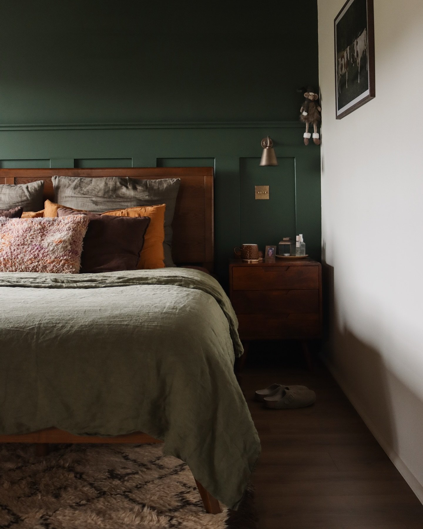Bedroom featuring a deep hunter green accent wall with wainscoting and a medium-toned wooden bed frame and nightstand.