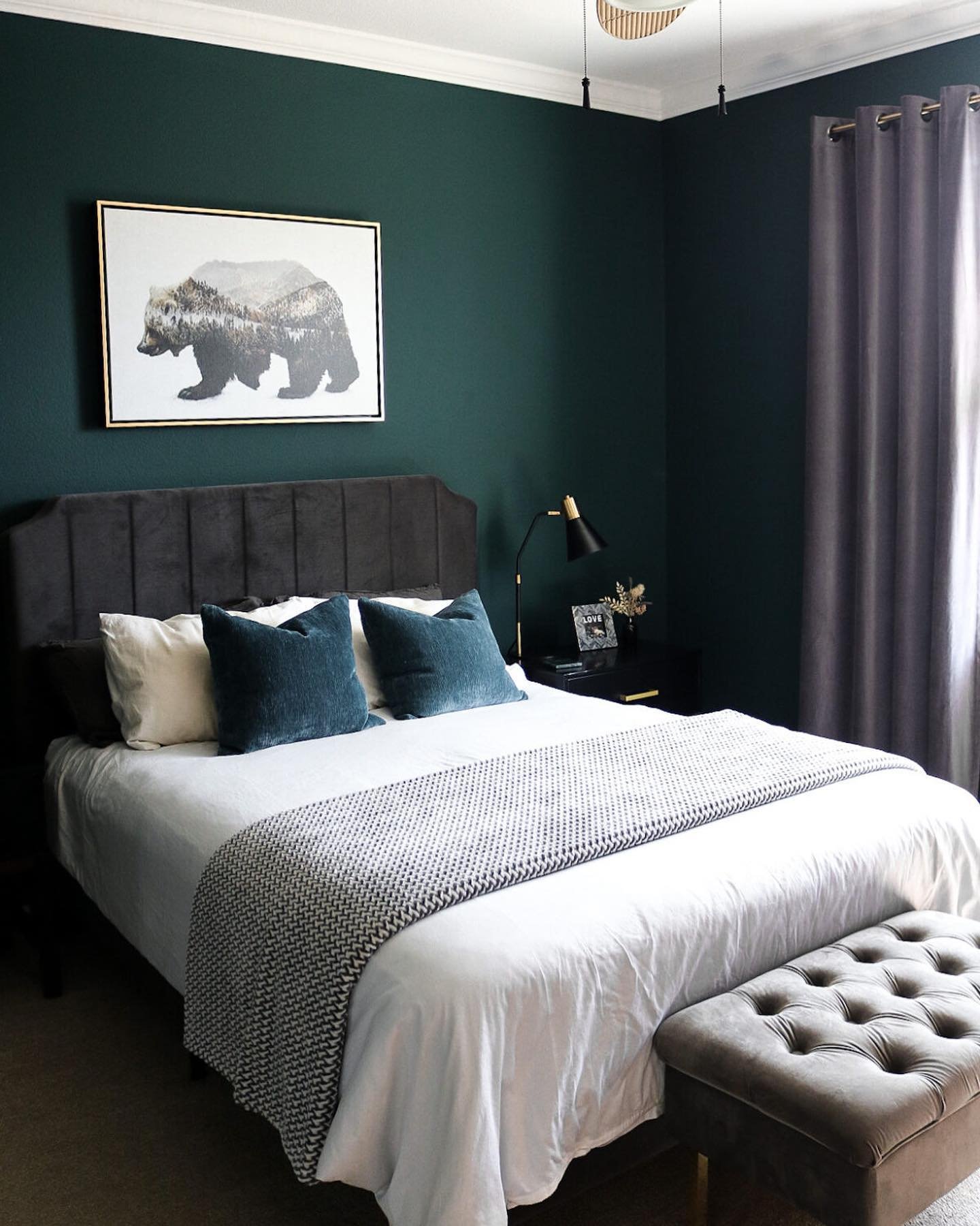 A sophisticated bedroom with a very dark green accent wall, a light tufted headboard, and mirrored nightstands with crystal lamps.