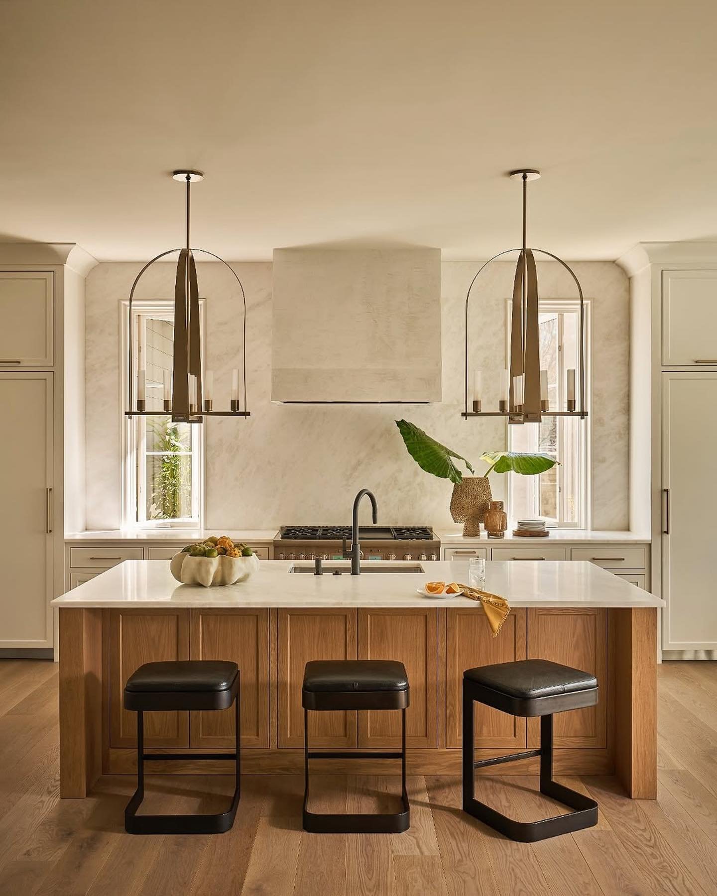 Luxury kitchen with a full slab white marble backsplash and surround, a textured integrated range hood, a wood island, and two bronze, arched chandelier pendants.