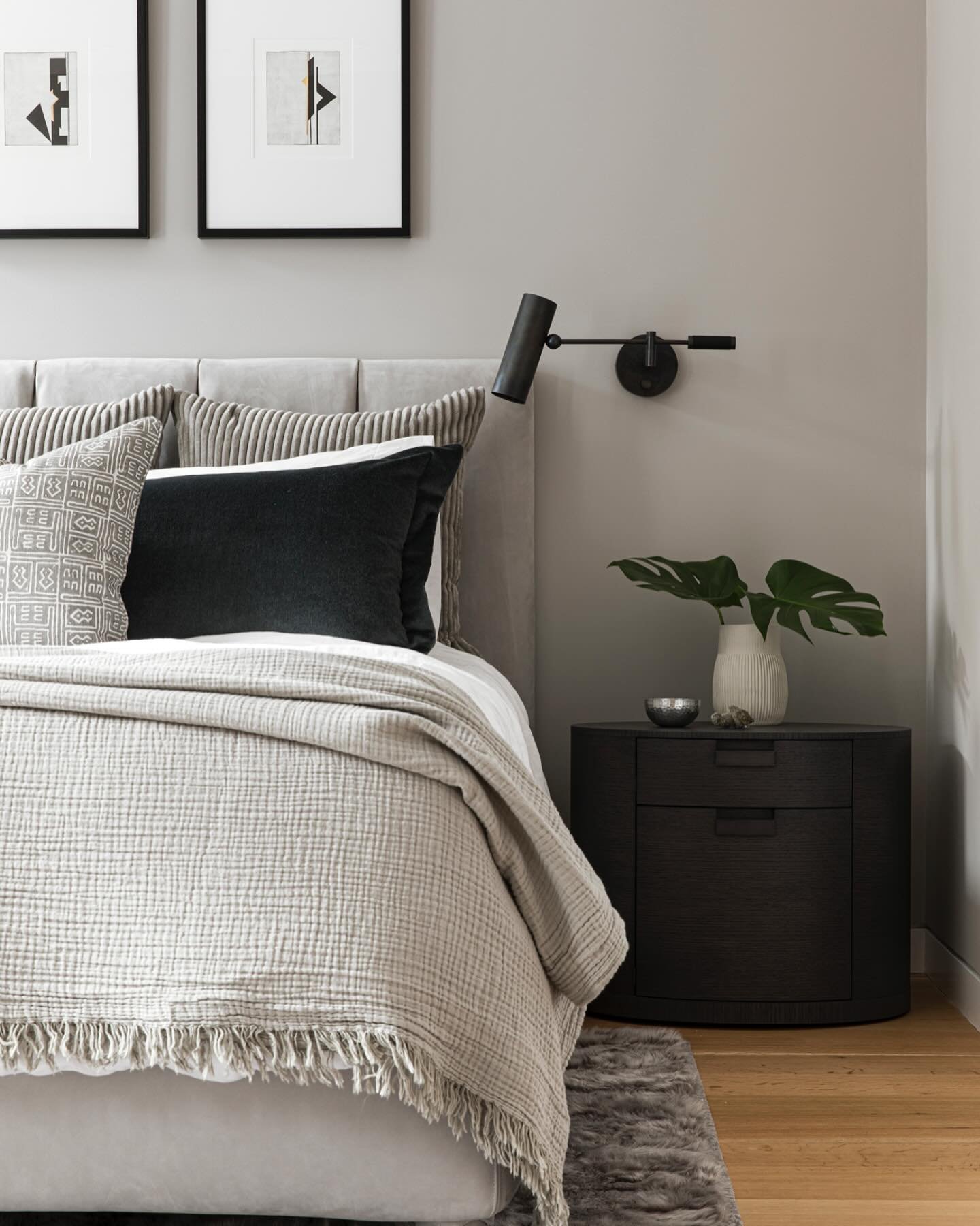 Dark wood nightstand with a smooth, rounded edge and two drawers, paired with a modern black wall-mounted sconce.