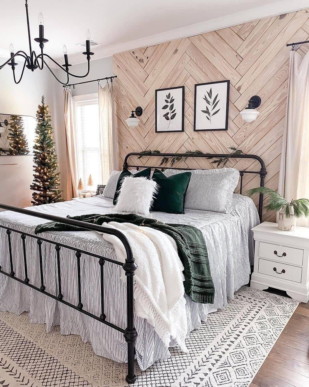 Farmhouse bedroom with a light wood chevron pattern accent wall and a black metal bed frame, accented with green pillows.