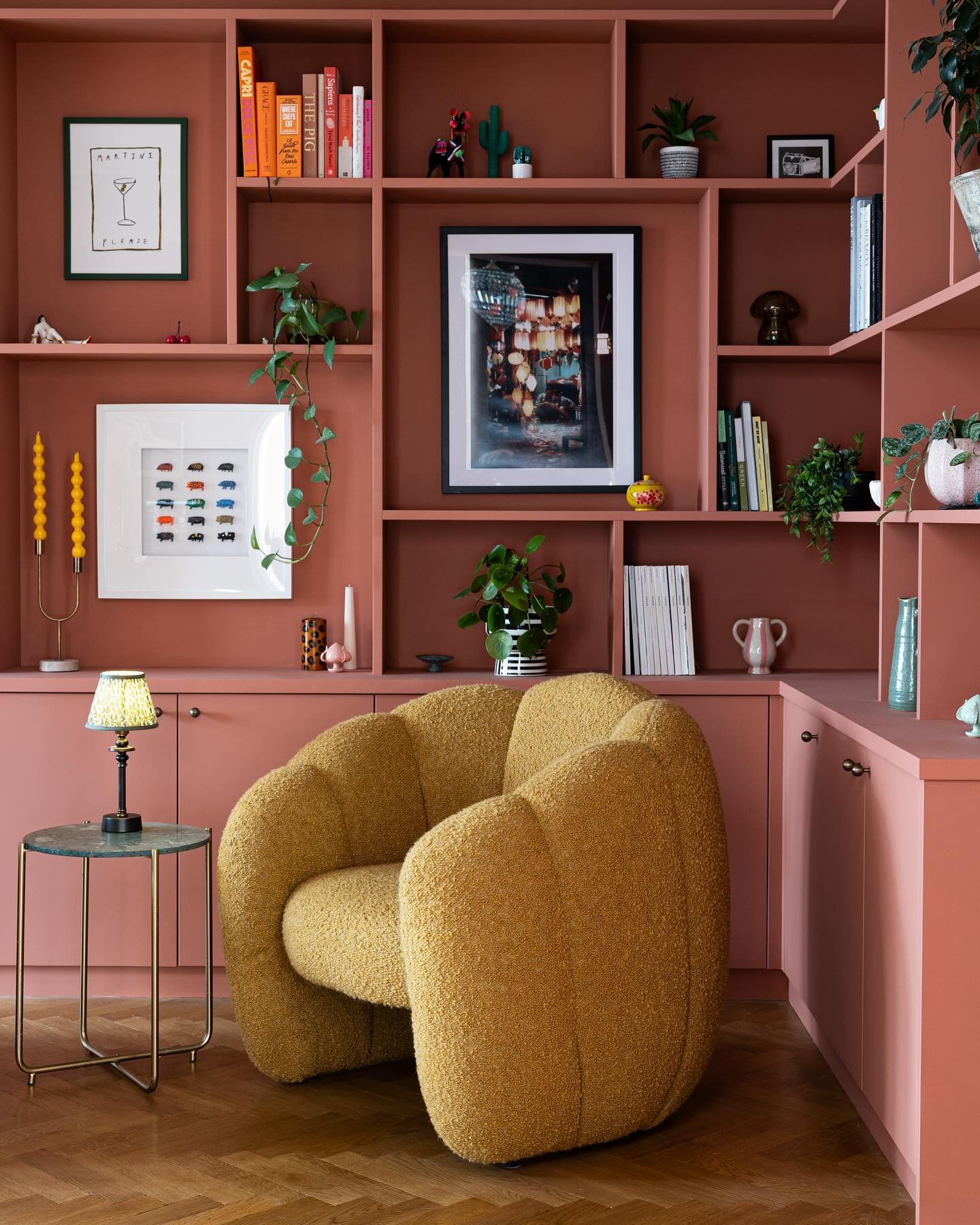 Vibrant reading nook with built-in bookshelves painted a dusty rose or terracotta pink, featuring a fuzzy mustard yellow contemporary armchair.