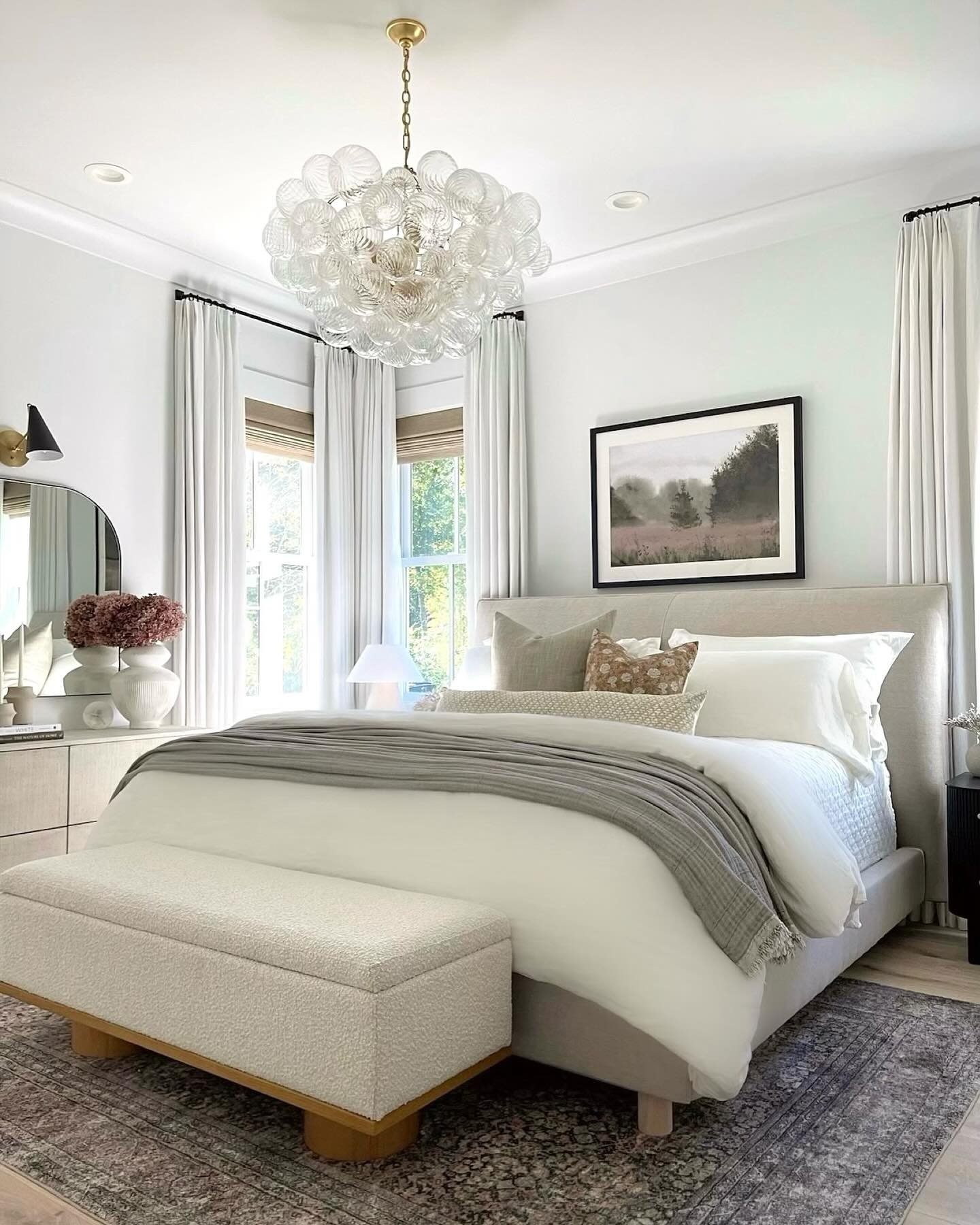 A light and elegant bedroom featuring a large bed with neutral bedding and a long, rectangular cream-colored bouclé storage ottoman bench.