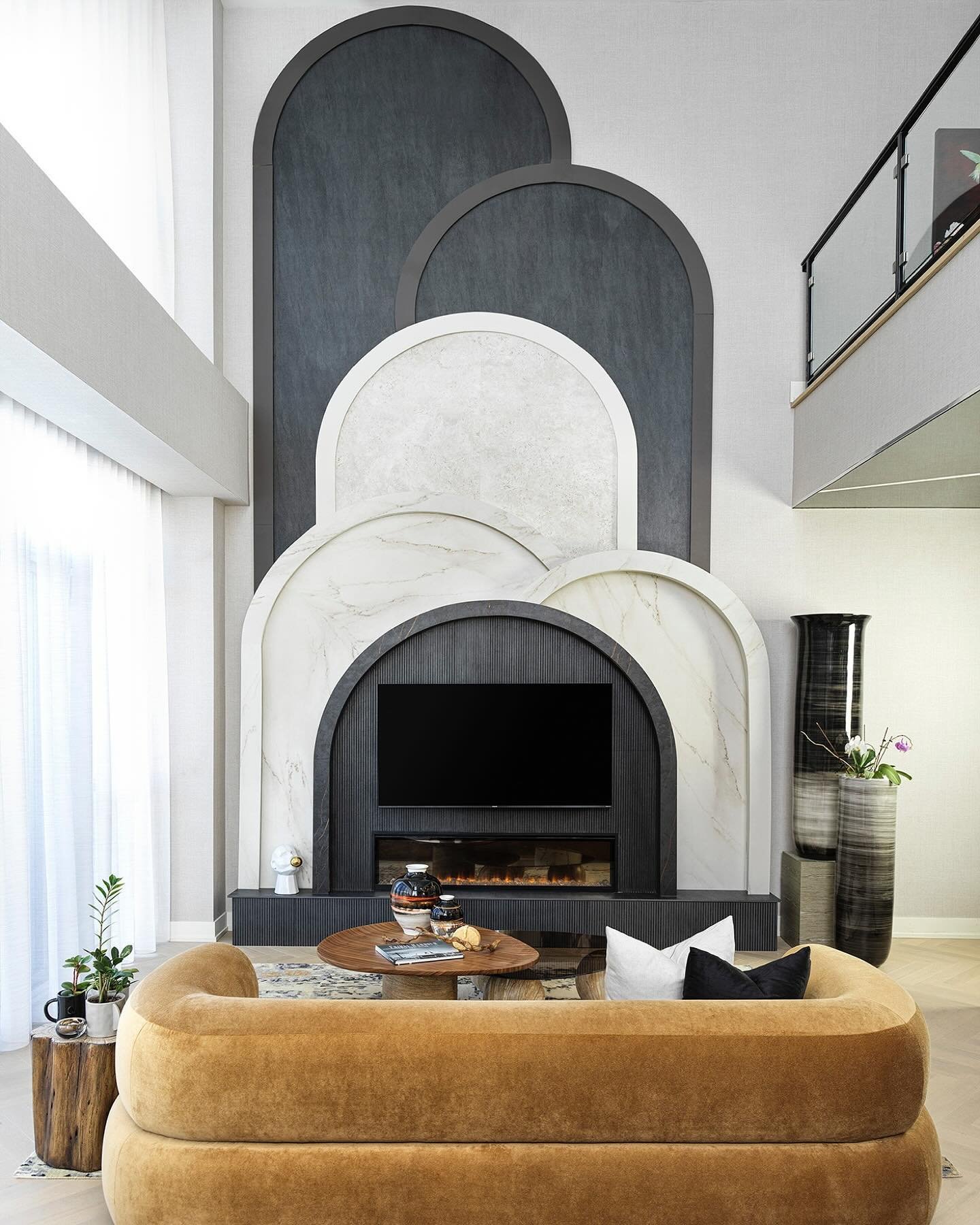 Modern living room with fireplace accent wall featuring layered arches in marble and slate textures.