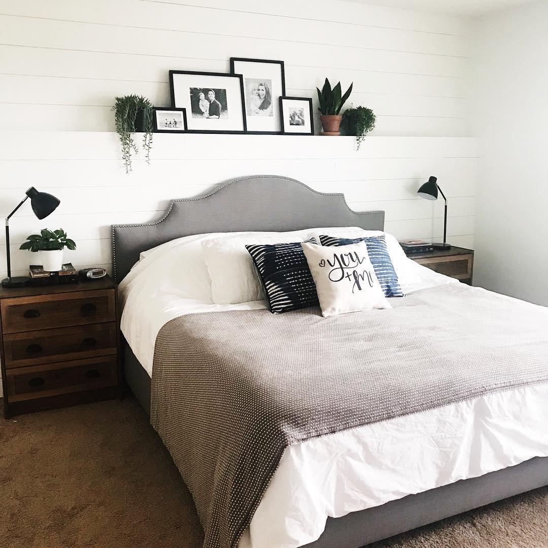 White shiplap wall ledge above bed with black photo frames and plants.
