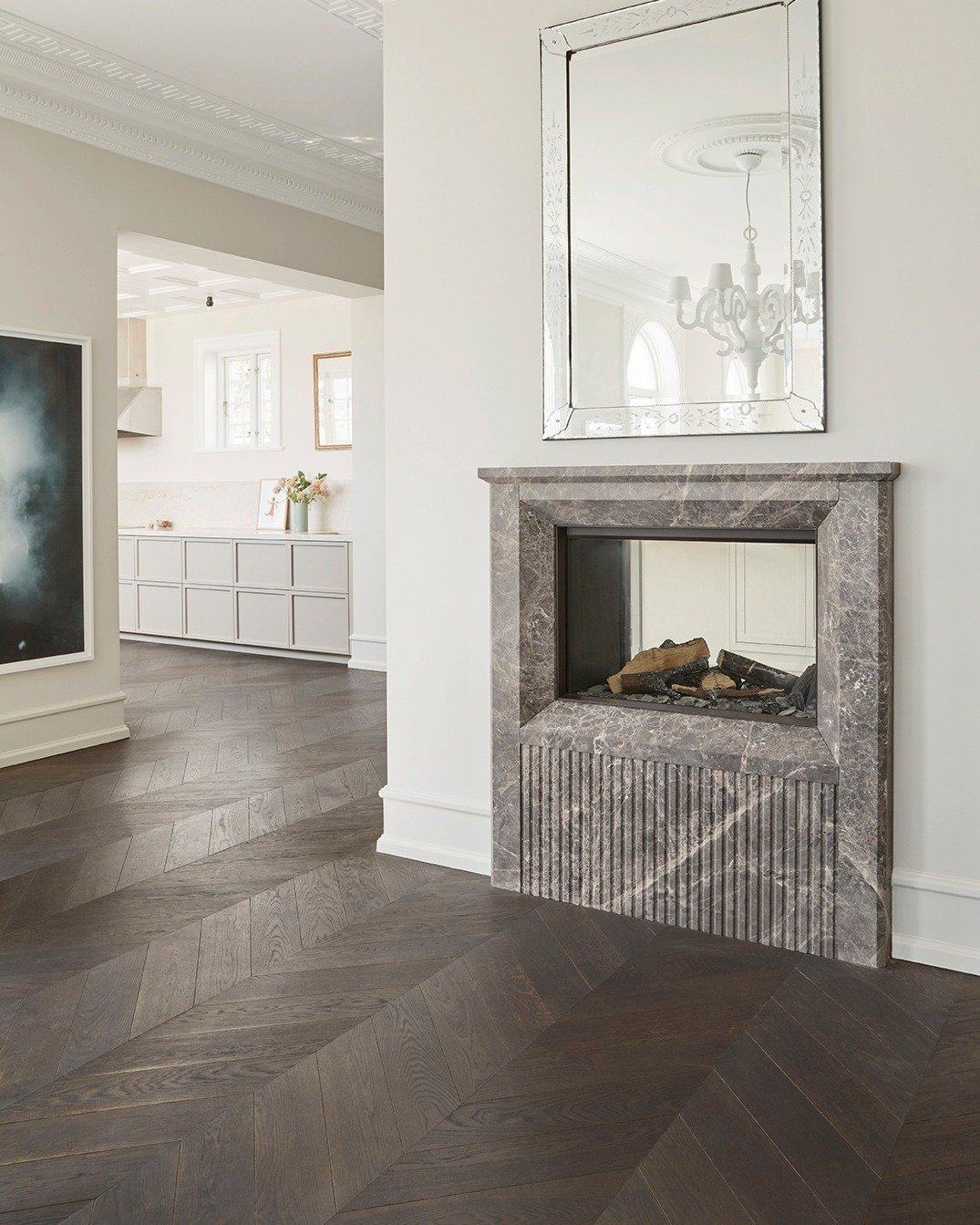 Modern fireplace surround made of striated grey marble with fluted paneling on the base, set against a white wall with a beveled mirror above.
