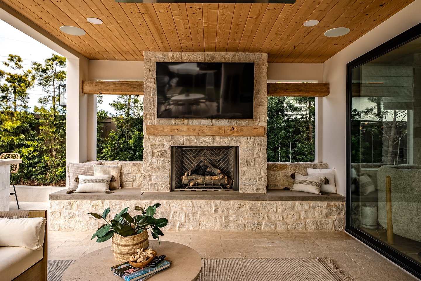 A built-in outdoor fireplace constructed with light, rustic stacked stone under a covered patio.
