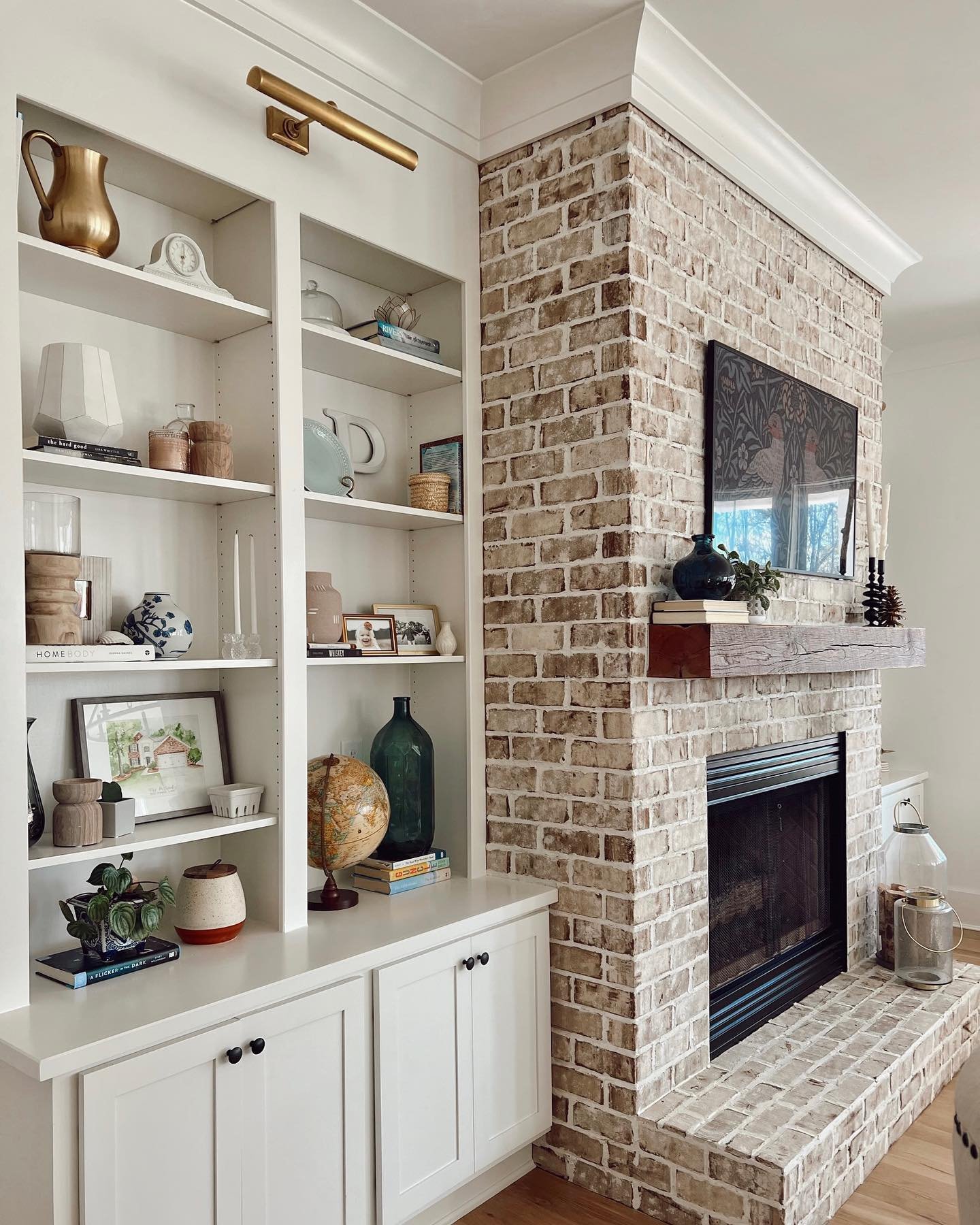 Floor-to-ceiling built-in white shelves with lower cabinets and gold lighting fixture.
