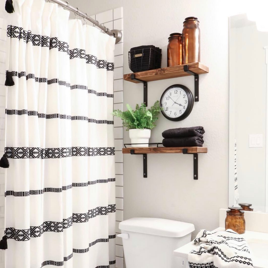 Two wooden shelves supported by black iron brackets holding amber jars and towels