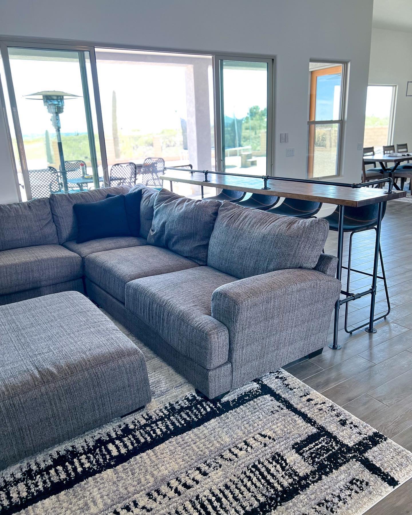 High top table with black pipe legs and bar stools behind a grey sectional sofa