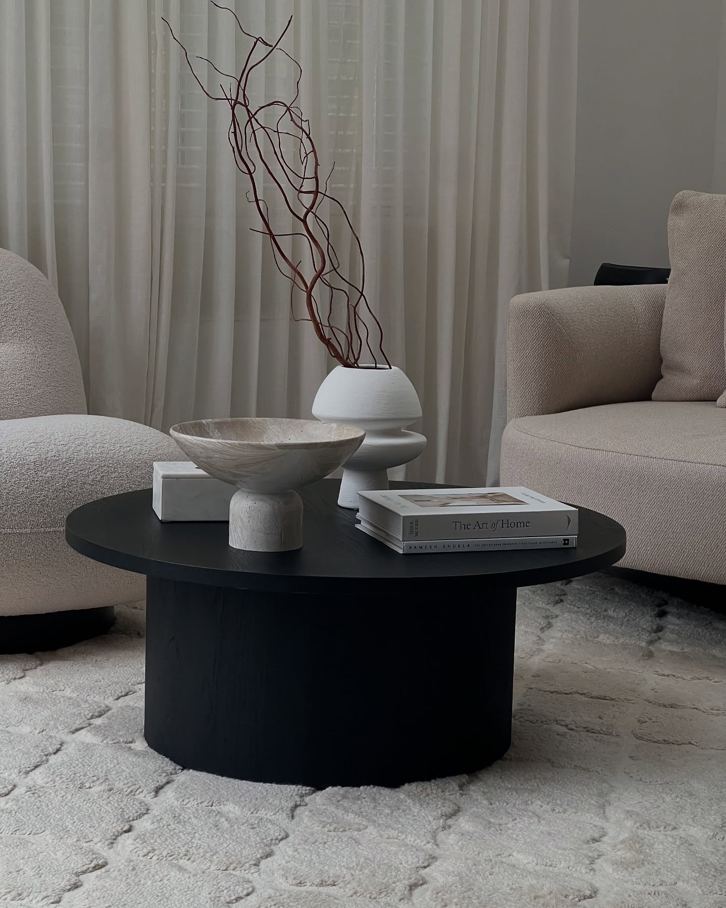 Round black coffee table with wide pedestal base in a neutral living room