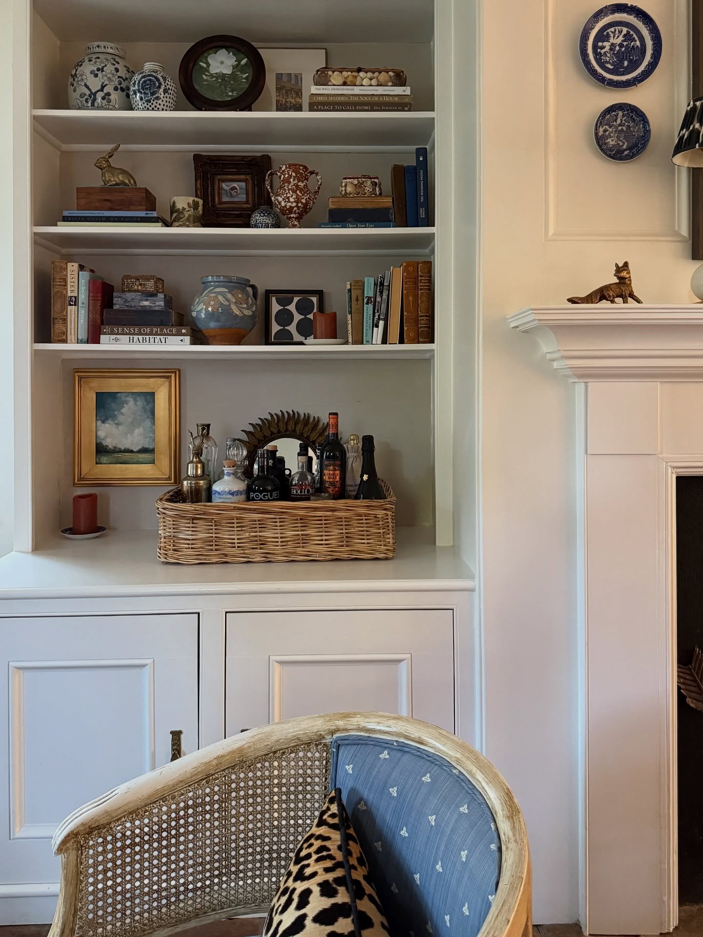 White built-in shelves featuring a wicker bar tray and vintage blue pottery.