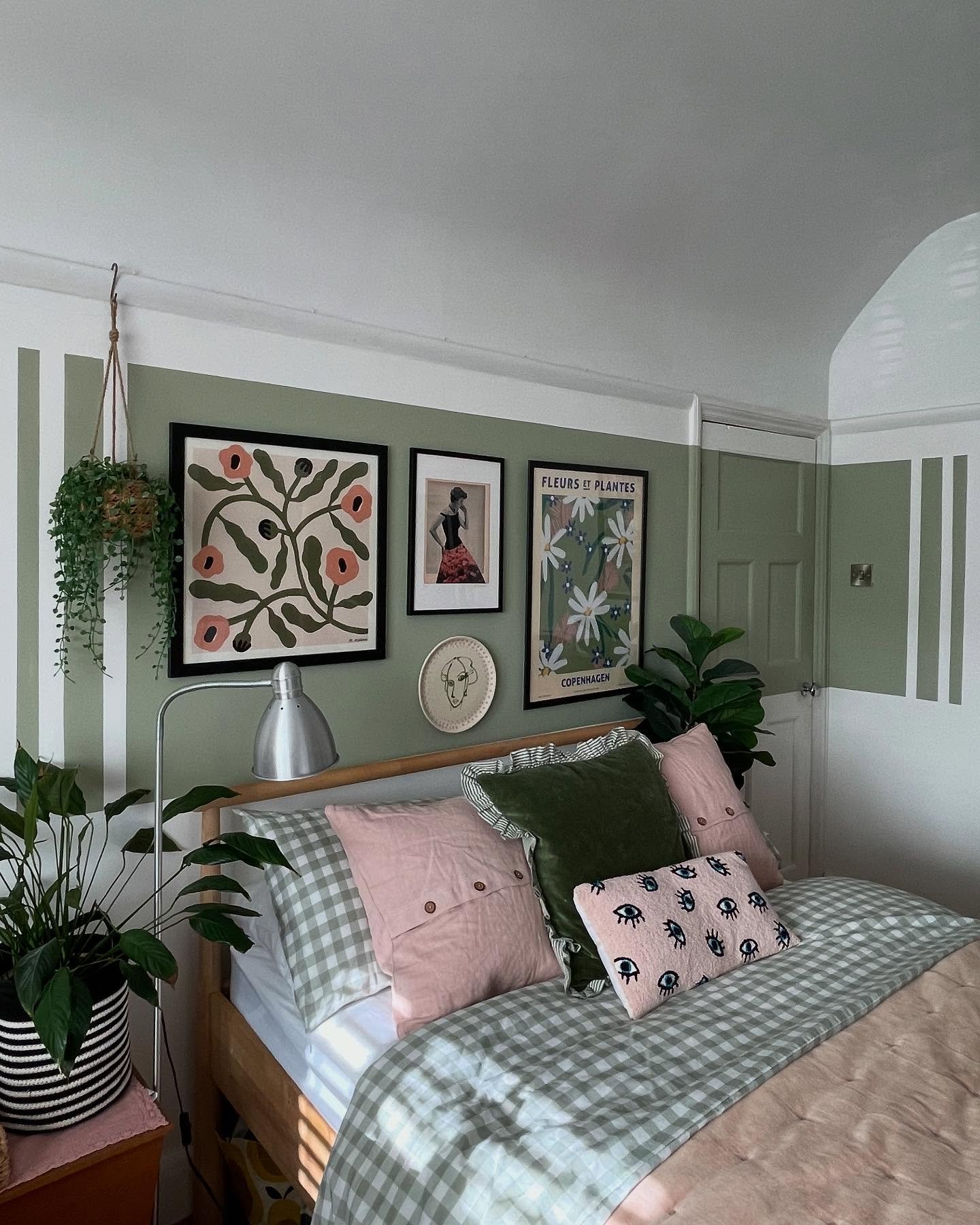 An eclectic bedroom featuring a sage green painted wall with vertical white stripes, checkered green and white bedding, and a gallery wall with bold botanical prints.